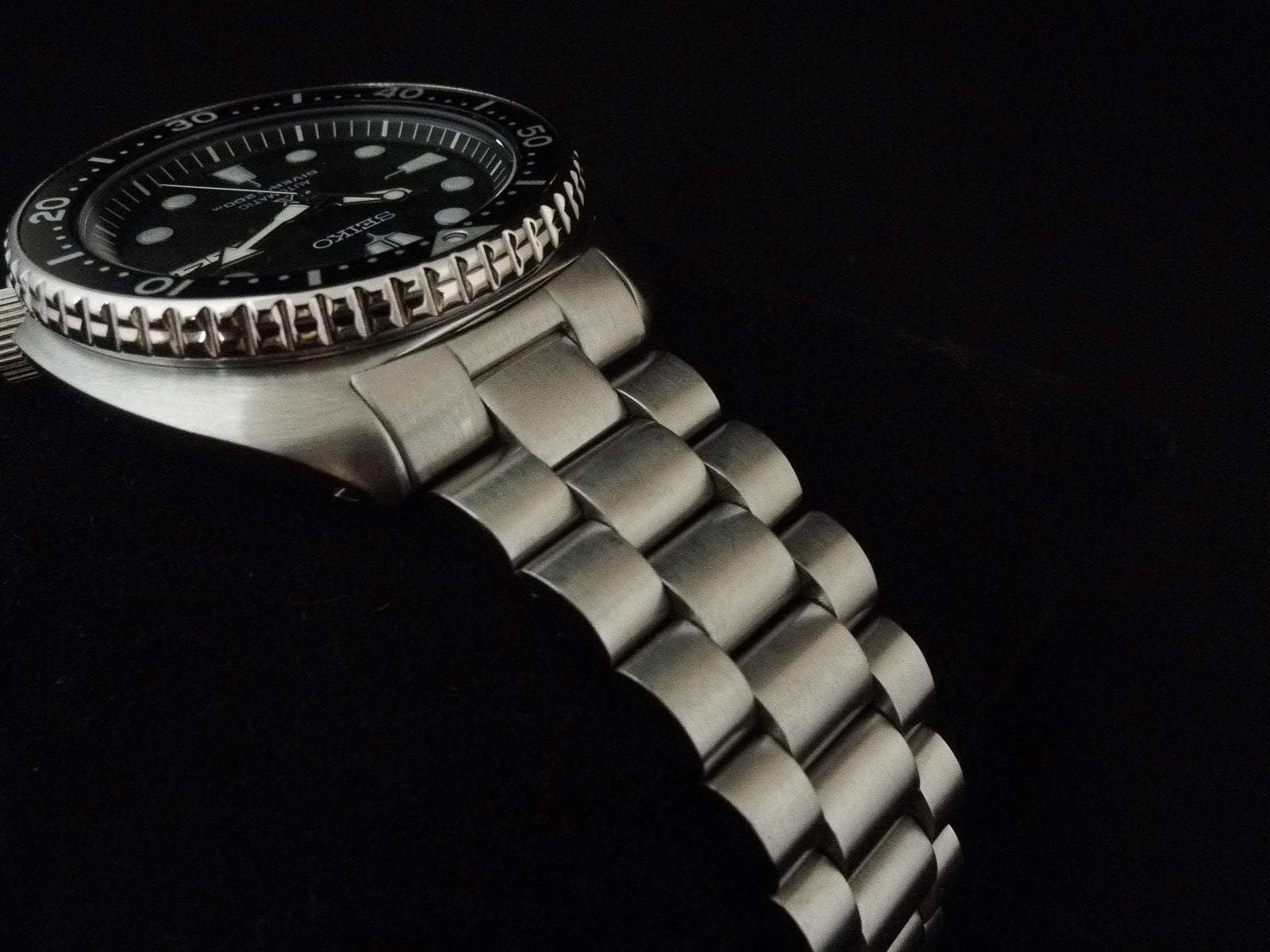 Seiko dive watch with black dial, luminous hour markers, stainless steel bracelet and rotating bezel on black background