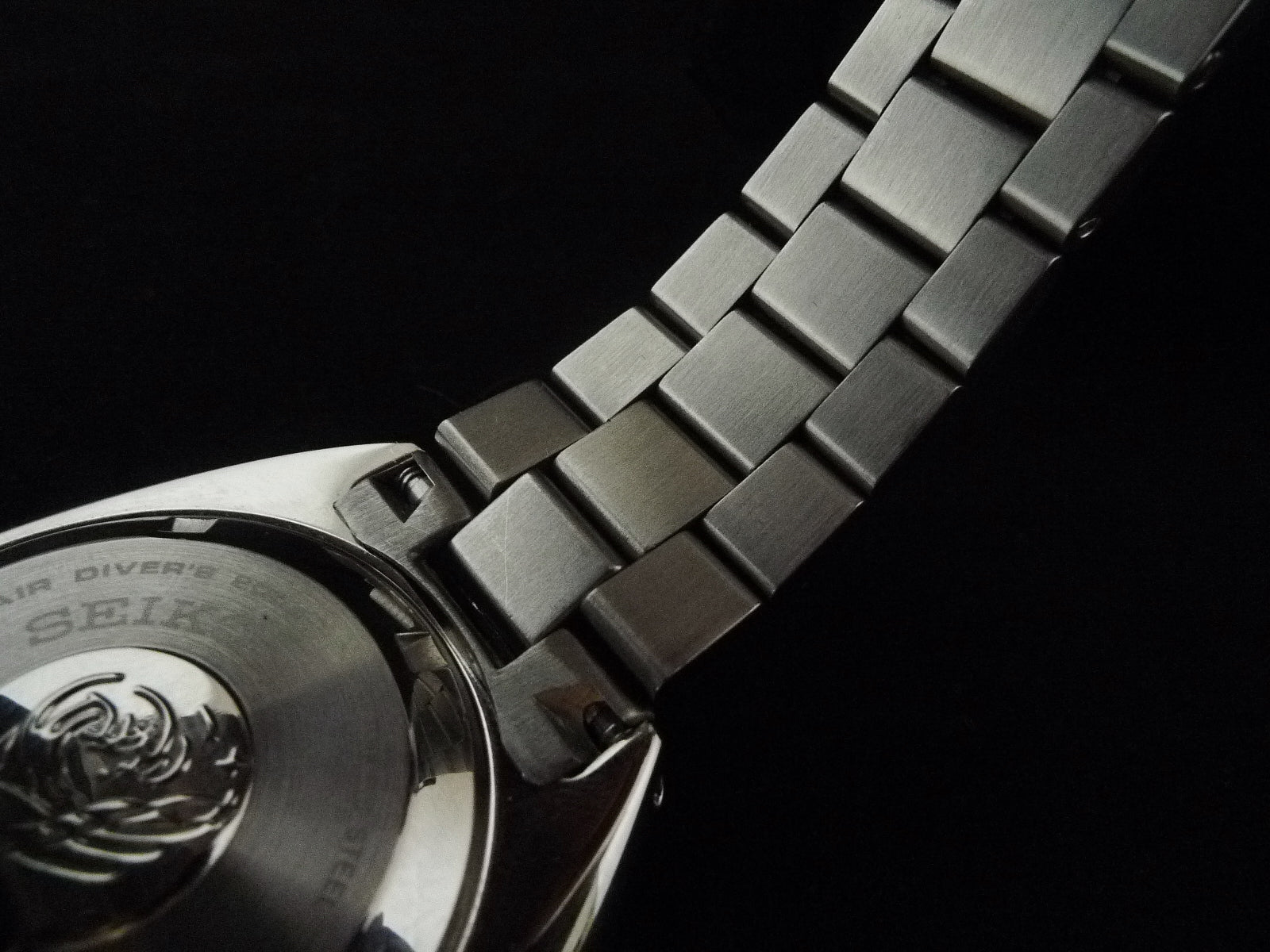 Stainless steel dive watch bracelet with brushed metal links and secure clasp, detail shot against black background