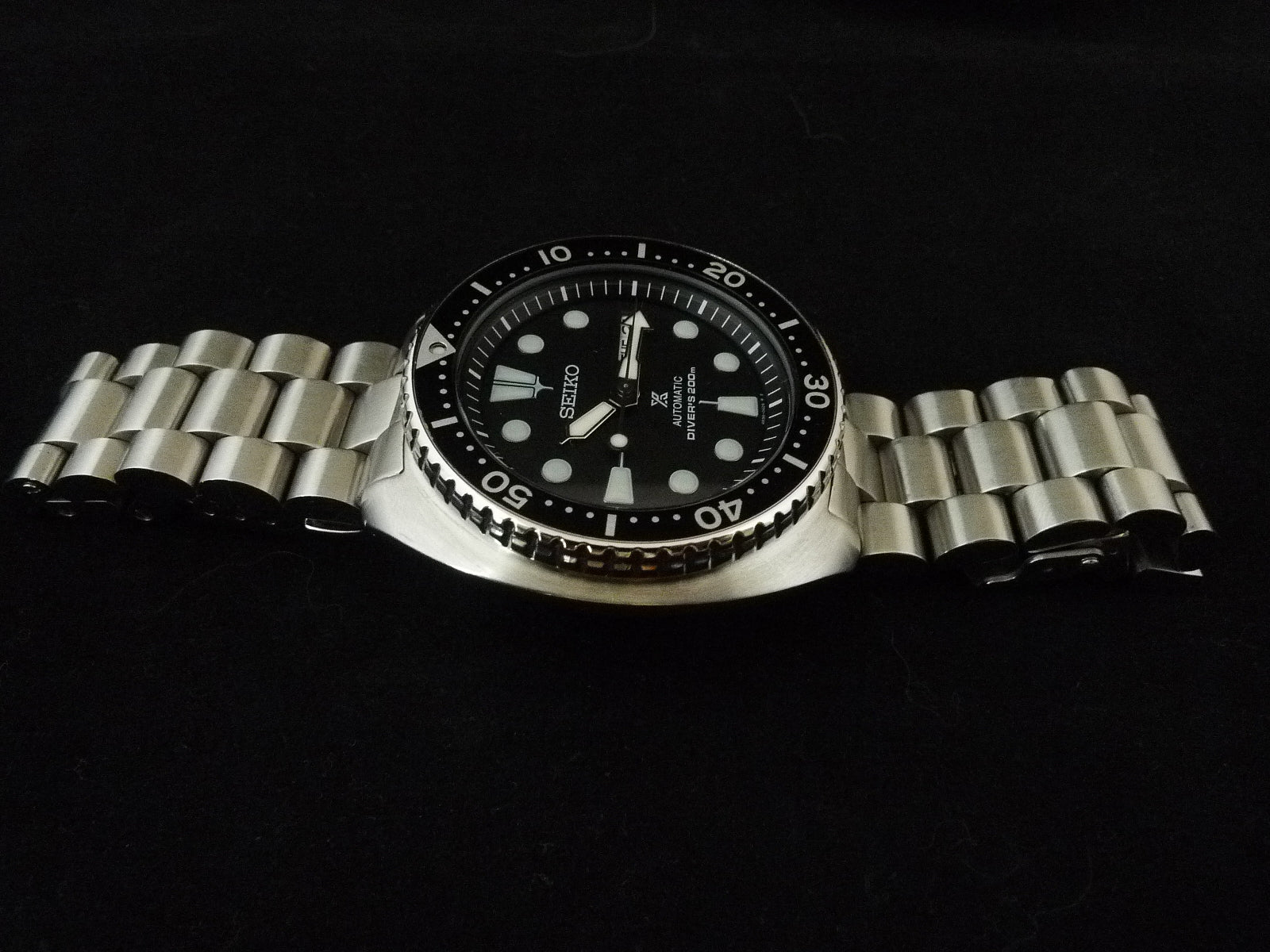 Seiko dive watch with black dial, stainless steel bracelet and rotating bezel on dark background