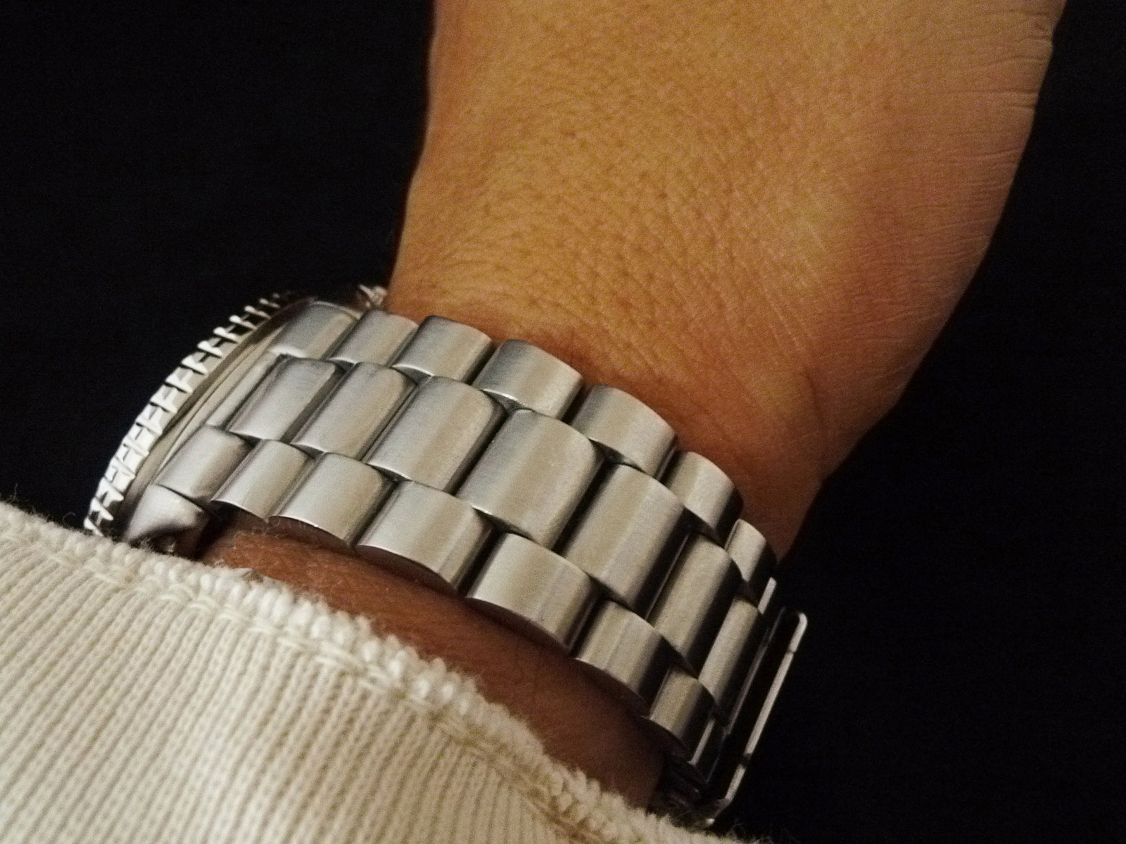 Stainless steel watch bracelet with polished solid links worn on wrist, showing metal construction and clasp detail