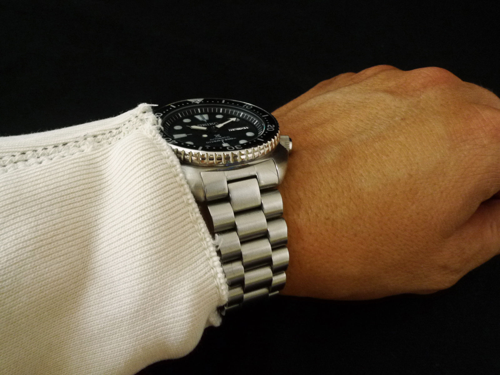 Seiko 6309 dive watch with black dial and rotating bezel on stainless steel bracelet, worn on wrist with white sleeve