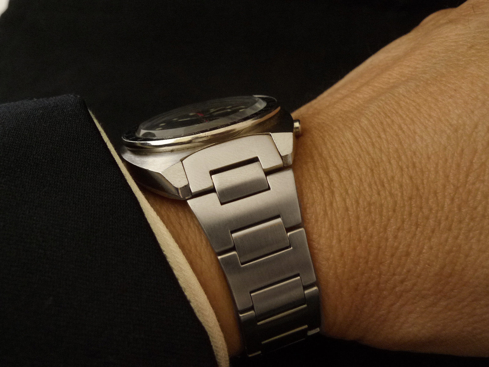 Silver tapered H-link metal bracelet watch with black dial worn on wrist, featuring brushed stainless steel links and polished accents