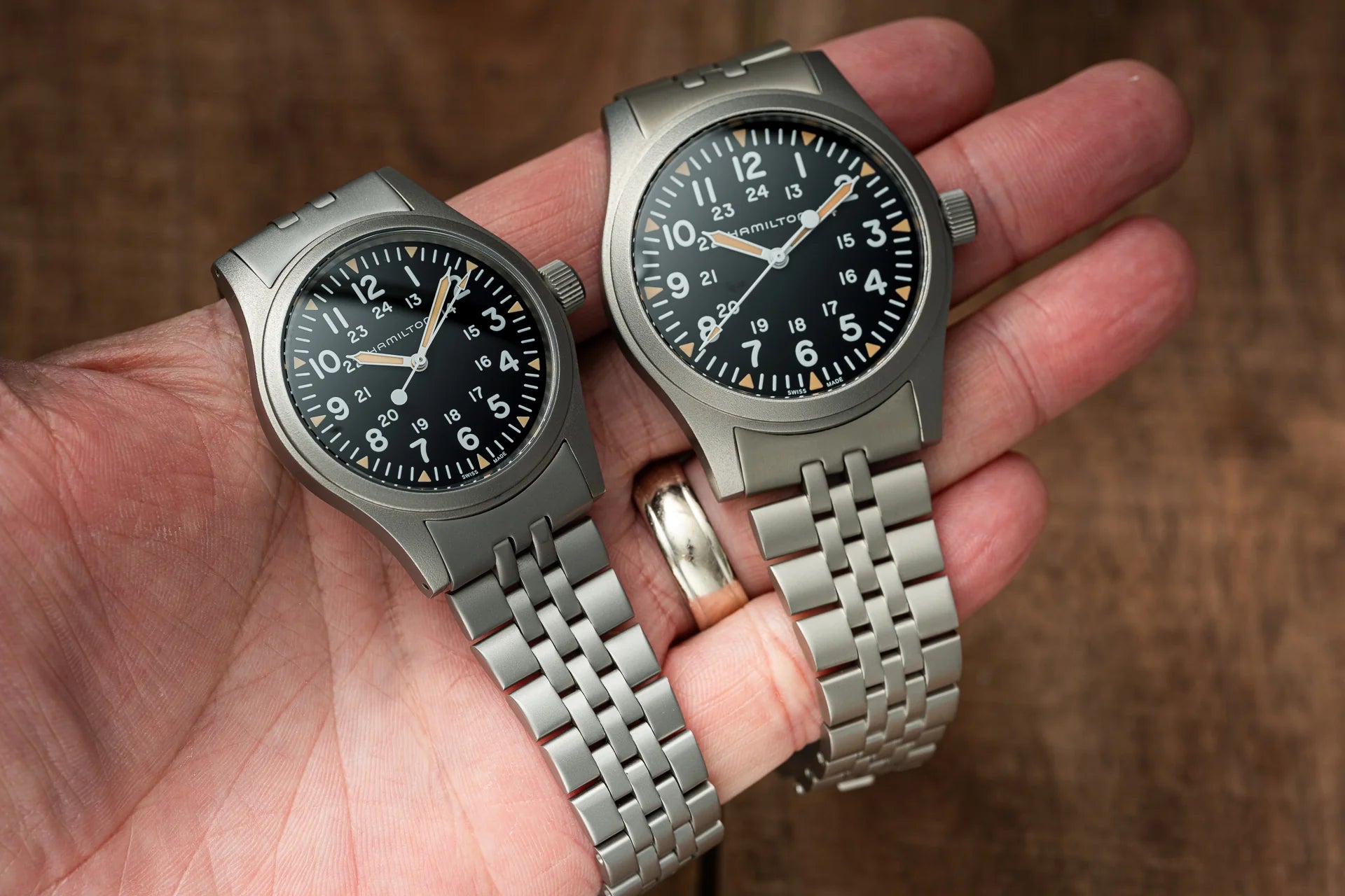 Two Hamilton Khaki mechanical watches with stainless steel bracelets and black dials displayed in hand
