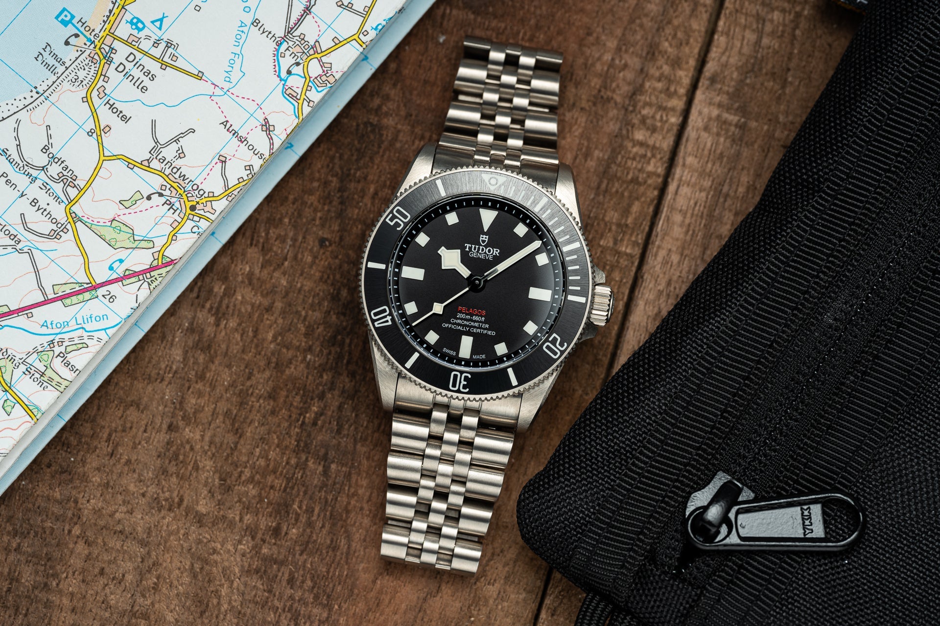 Tudor Pelagos 39mm dive watch with stainless steel bracelet on wooden surface next to map and carabiner
