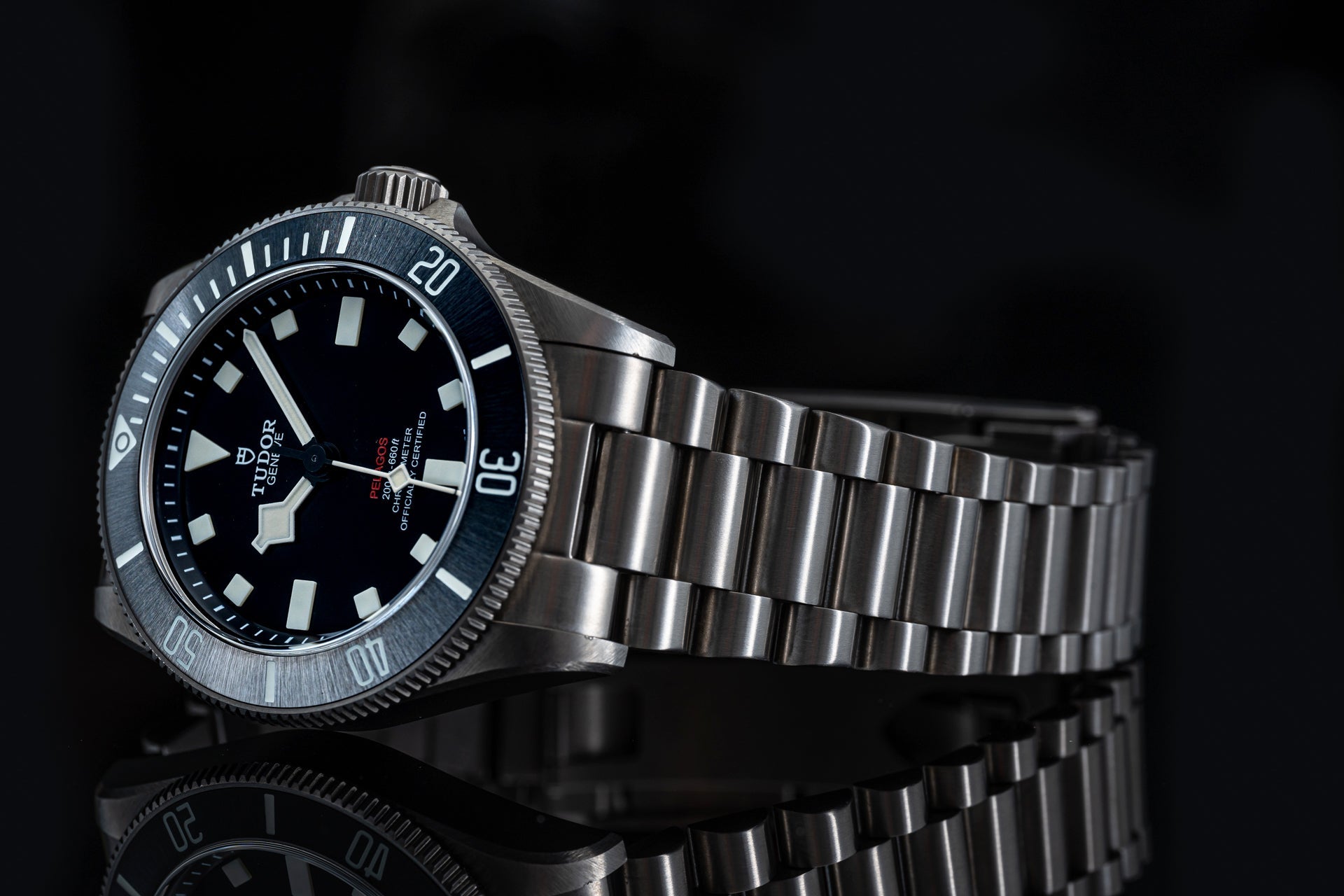 Titanium dive watch with black dial, white markers, rotating bezel and stainless steel bracelet on black background