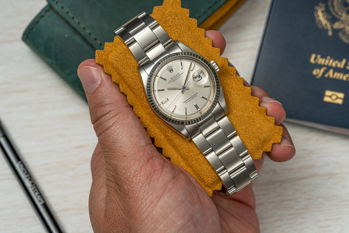 Vintage Rolex Datejust stainless steel bracelet with oyster links and date window, held in hand with passport background