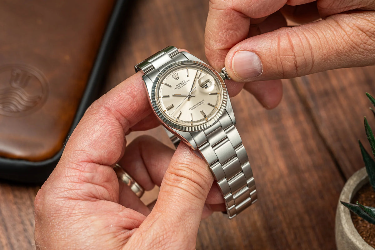 Vintage Rolex Datejust stainless steel watch with cream dial held in hand, showcasing classic three-link bracelet design