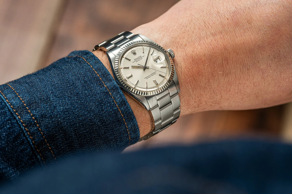 Vintage Rolex Datejust 1601 stainless steel watch with fluted bezel and date window on wrist with denim cuff