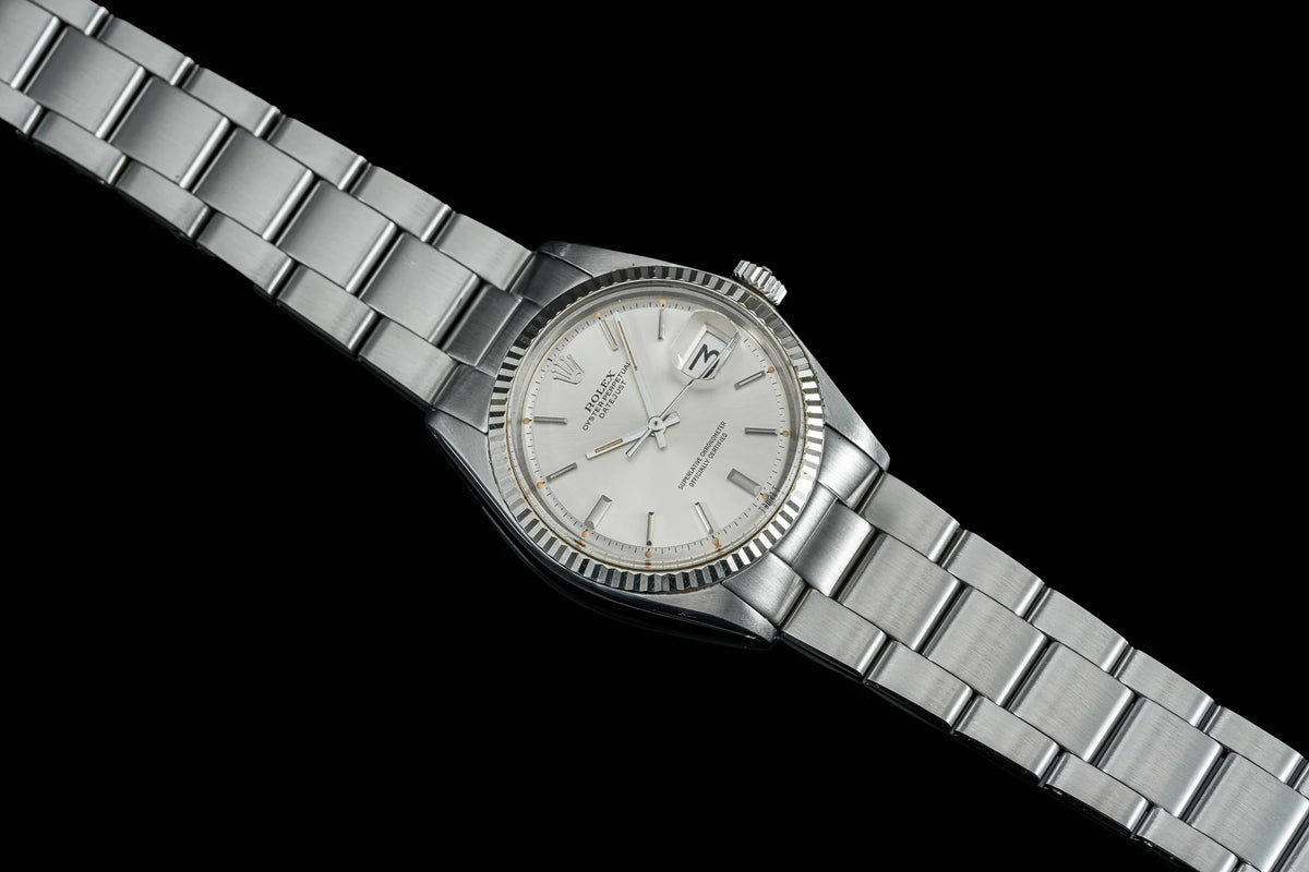 Vintage Rolex Datejust stainless steel watch with fluted bezel, silver dial, and three-link bracelet on black background