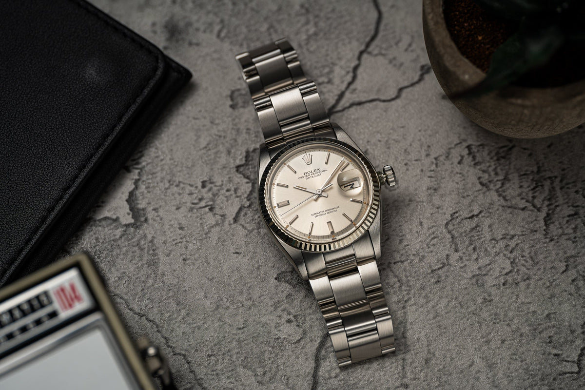 Vintage Rolex Datejust stainless steel watch with fluted bezel and cream dial on gray textured background
