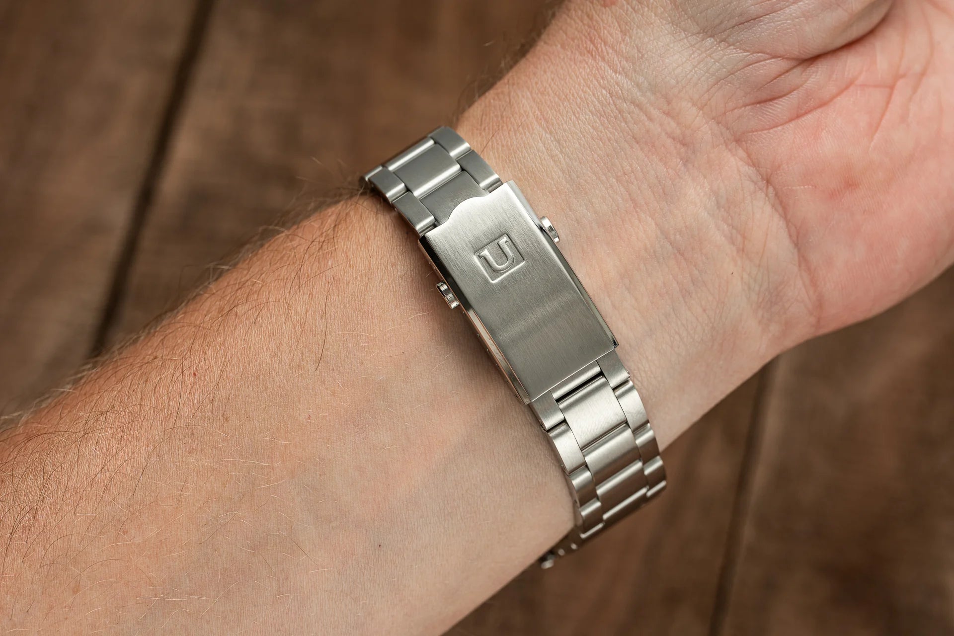 Stainless steel watch bracelet with polished and brushed links worn on wrist, featuring branded clasp