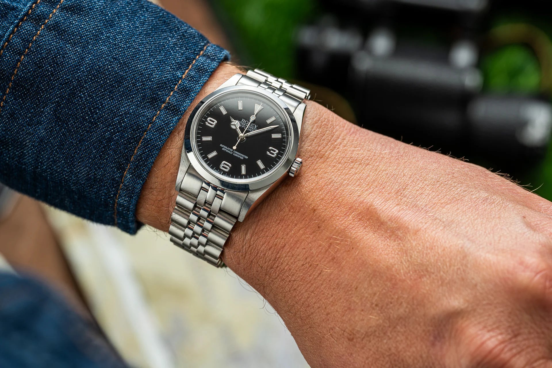 Stainless steel Rolex Explorer watch with black dial on men's wrist wearing denim and cream shirt
