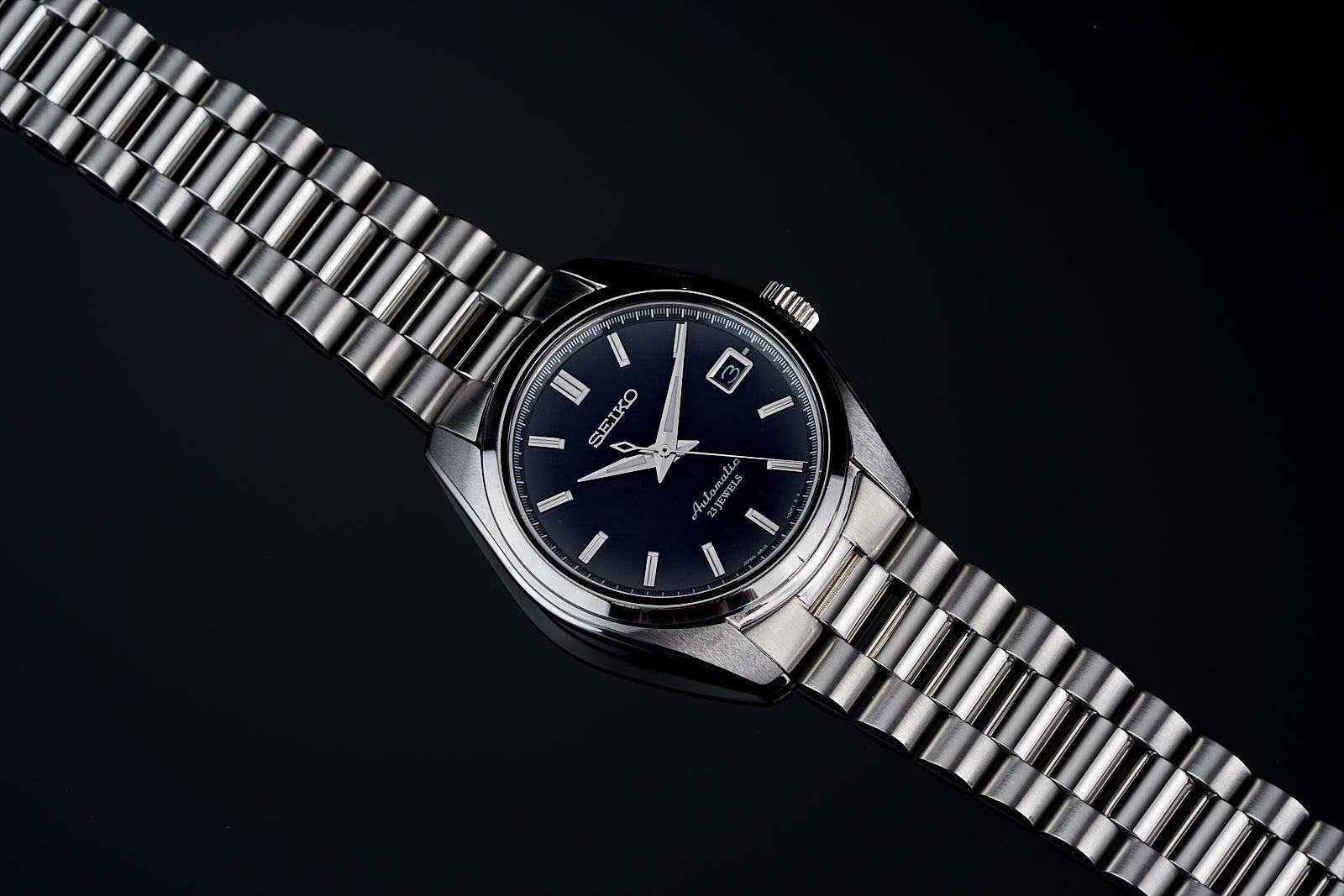 Seiko Prospex stainless steel watch with dark blue dial, date window, and matching metal bracelet on black background