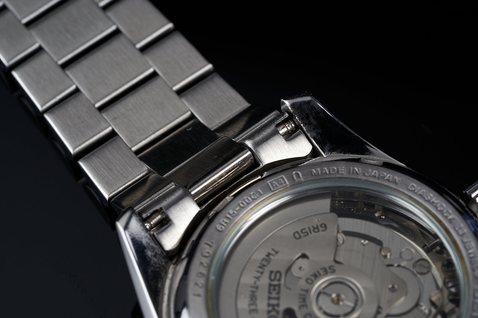 Seiko automatic watch with stainless steel bracelet and caseback detail showing Japanese movement mechanism