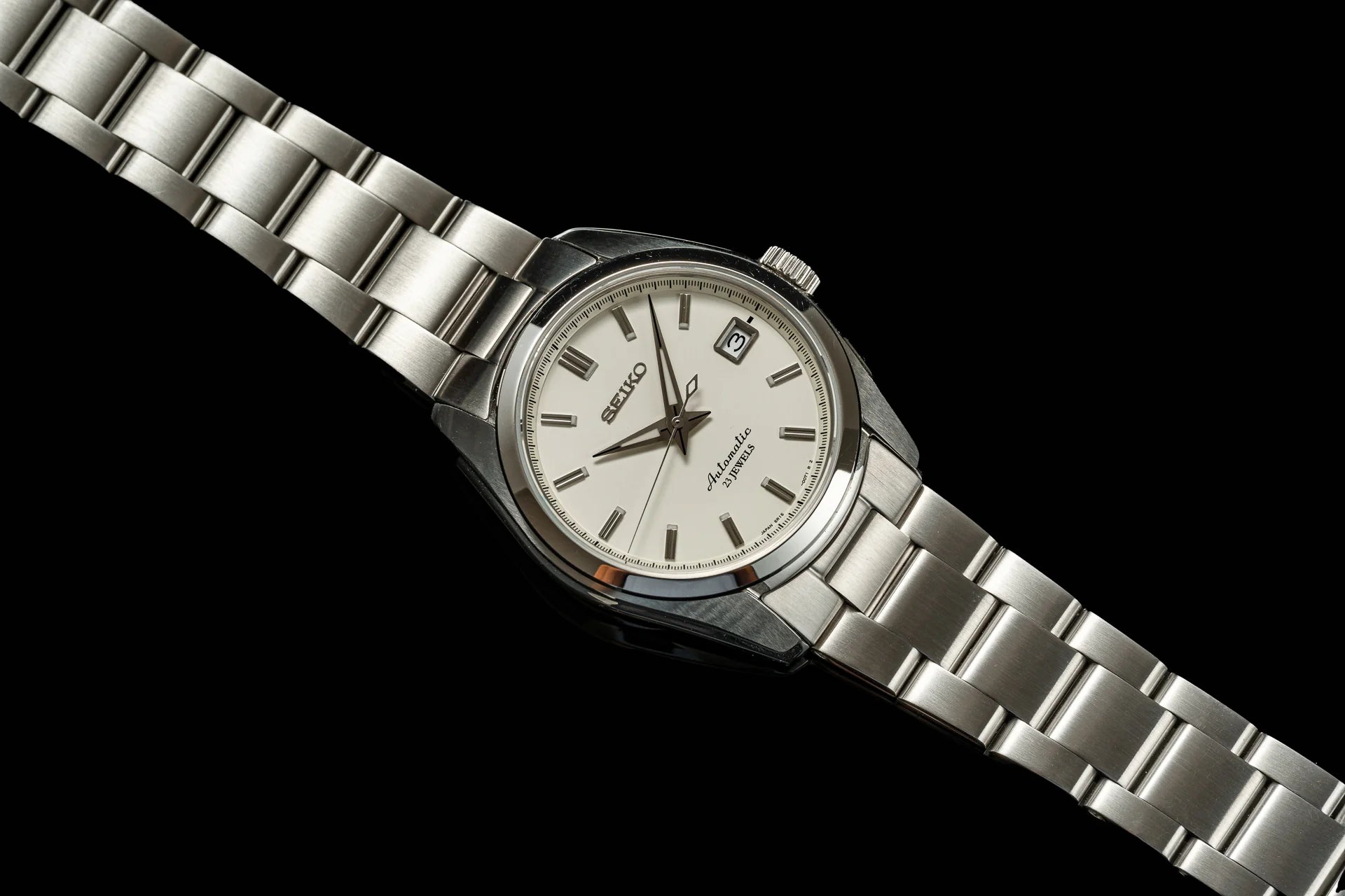 Seiko automatic watch with stainless steel bracelet, cream dial, date window, and Roman numeral hour markers on black background