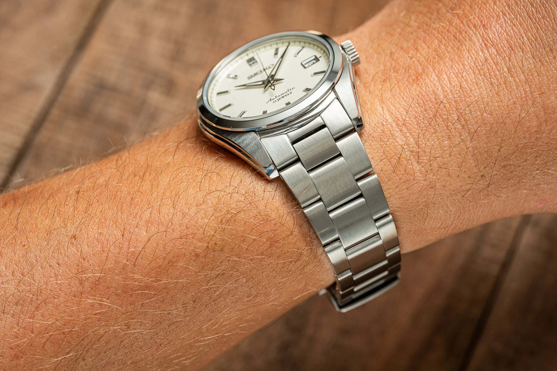 Silver stainless steel automatic watch with cream dial and metal bracelet worn on wrist