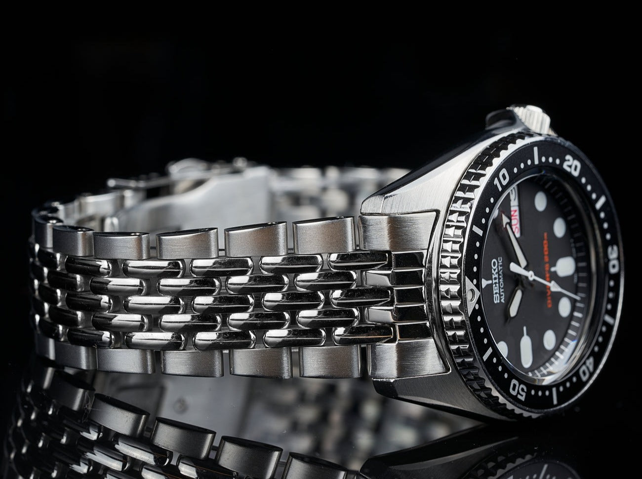 Seiko SKX013 dive watch with black dial and stainless steel beads of rice bracelet on black background