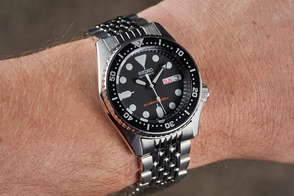 Seiko SKX013 automatic dive watch with black dial, stainless steel beads of rice bracelet, day-date window, worn on wrist