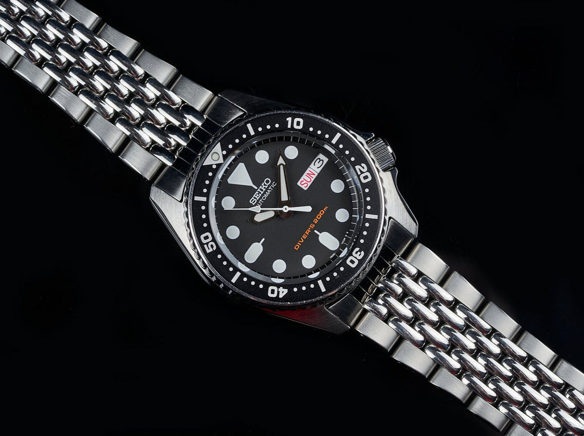 Seiko SKX013 dive watch with stainless steel beads of rice bracelet, black dial, and luminous hour markers on black background