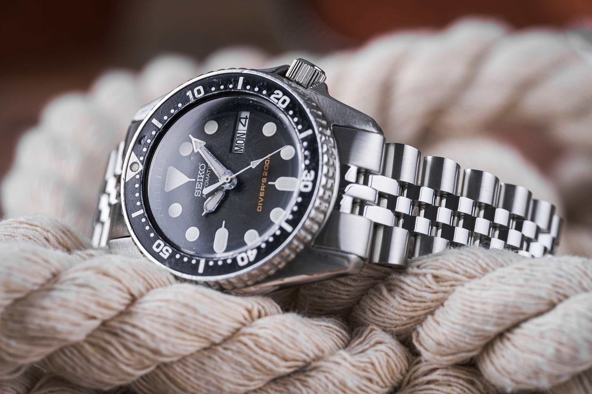 Seiko Diver's 200M stainless steel watch with black dial, day-date window, and jubilee bracelet on nautical rope