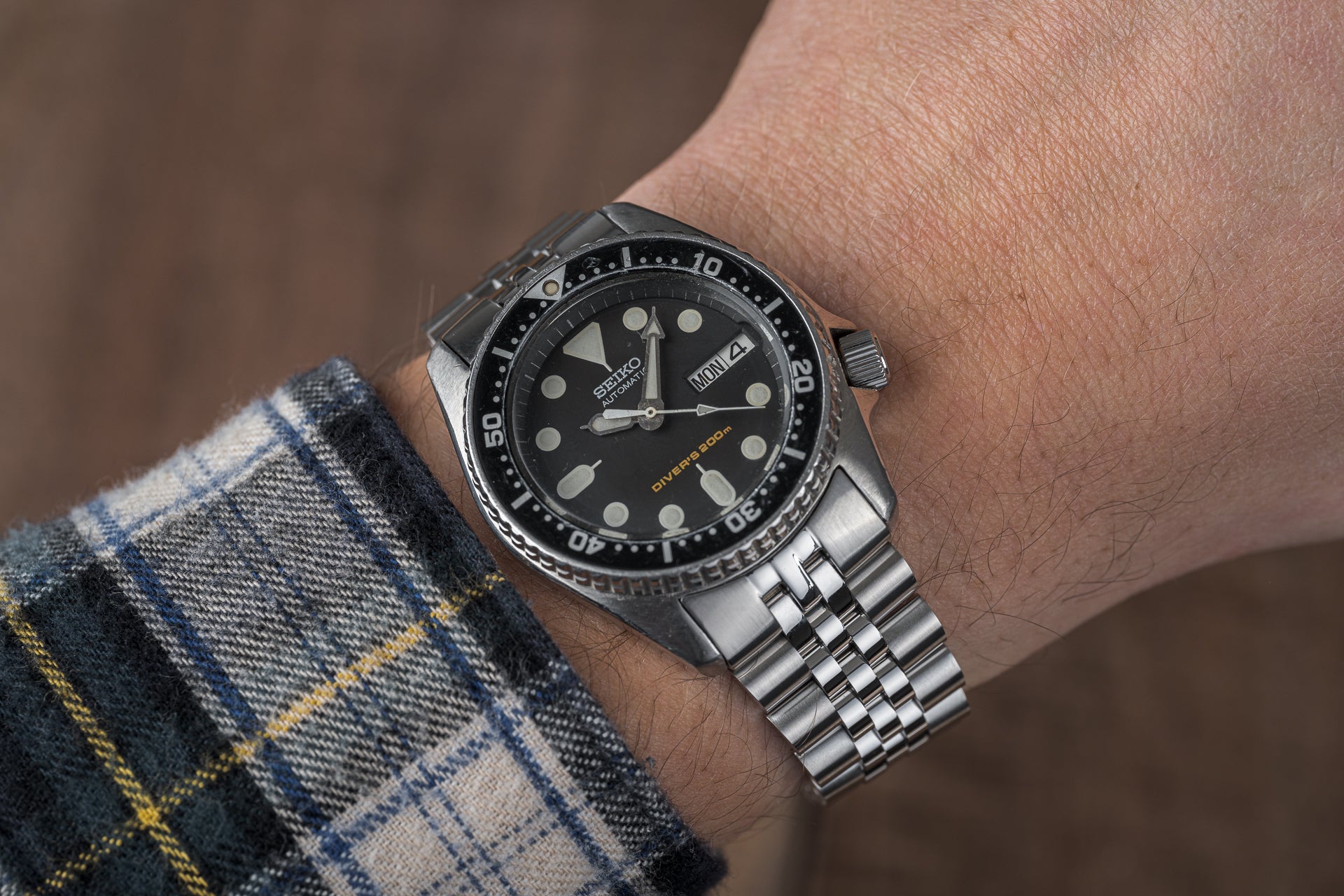 Seiko SKX013 dive watch with black dial, stainless steel bracelet and bezel on wrist wearing plaid shirt