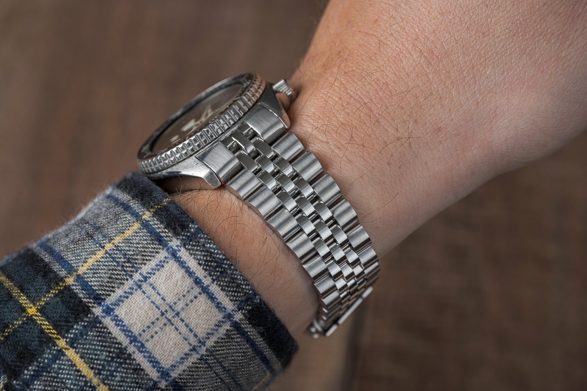 Silver stainless steel bracelet with solid link band worn on wrist with plaid shirt sleeve visible