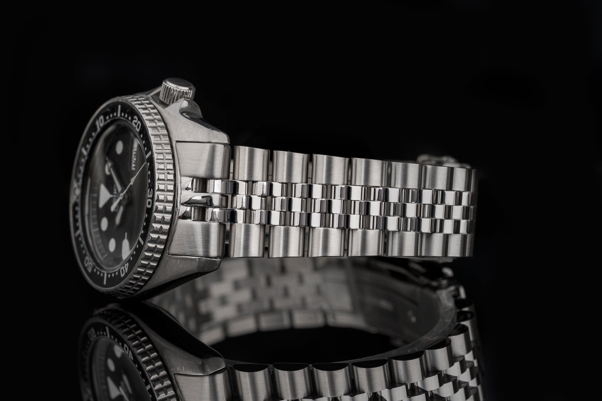 Stainless steel dive watch with black dial and metal bracelet on black background, side profile view