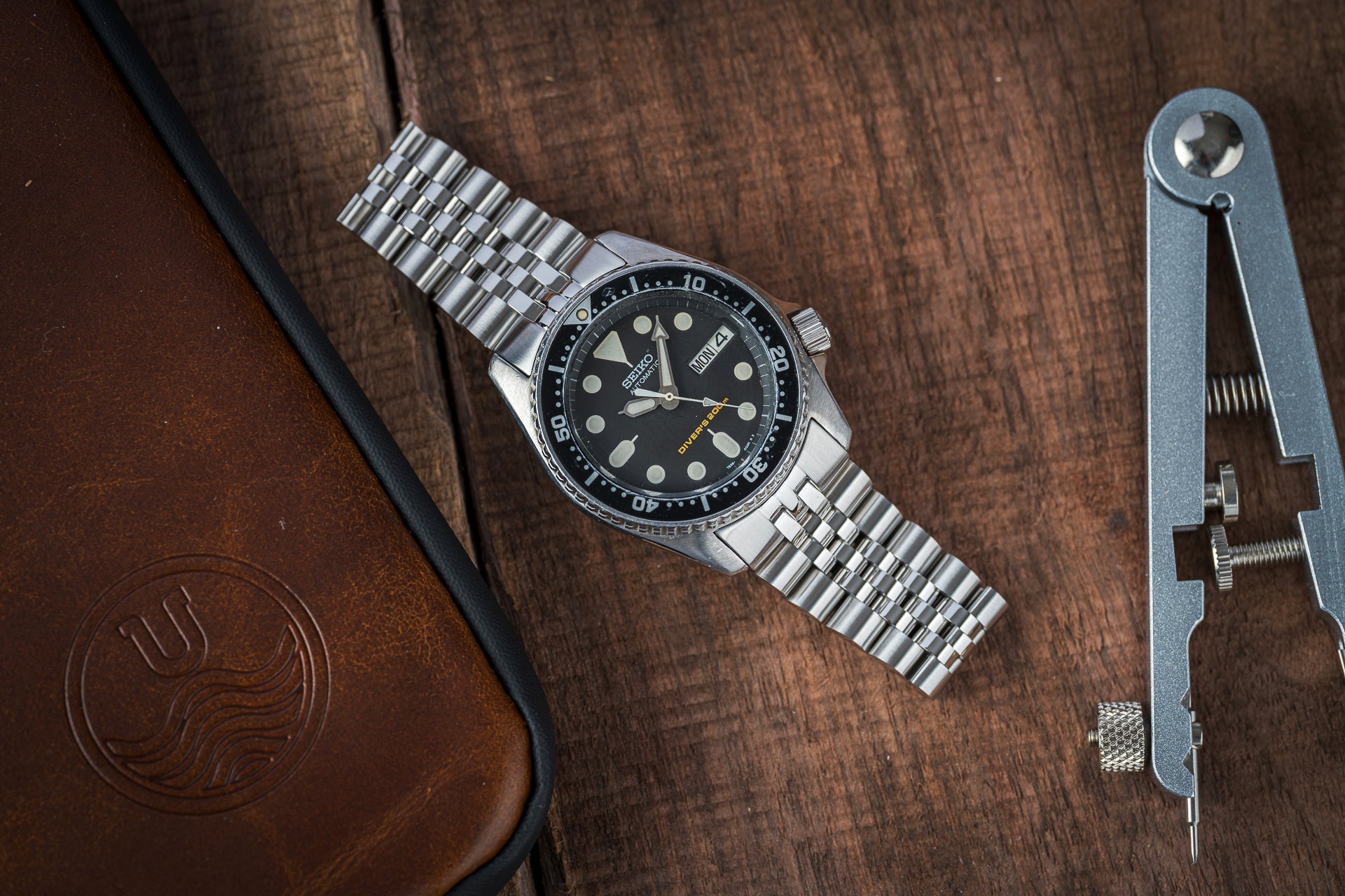 Seiko SKX013 executive dive watch with black dial and stainless steel bracelet on wooden surface next to vintage tool