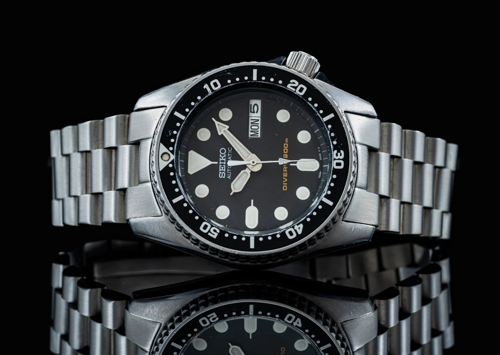 Seiko SKX013 automatic diver watch with stainless steel bracelet, black dial, and day-date window on black background