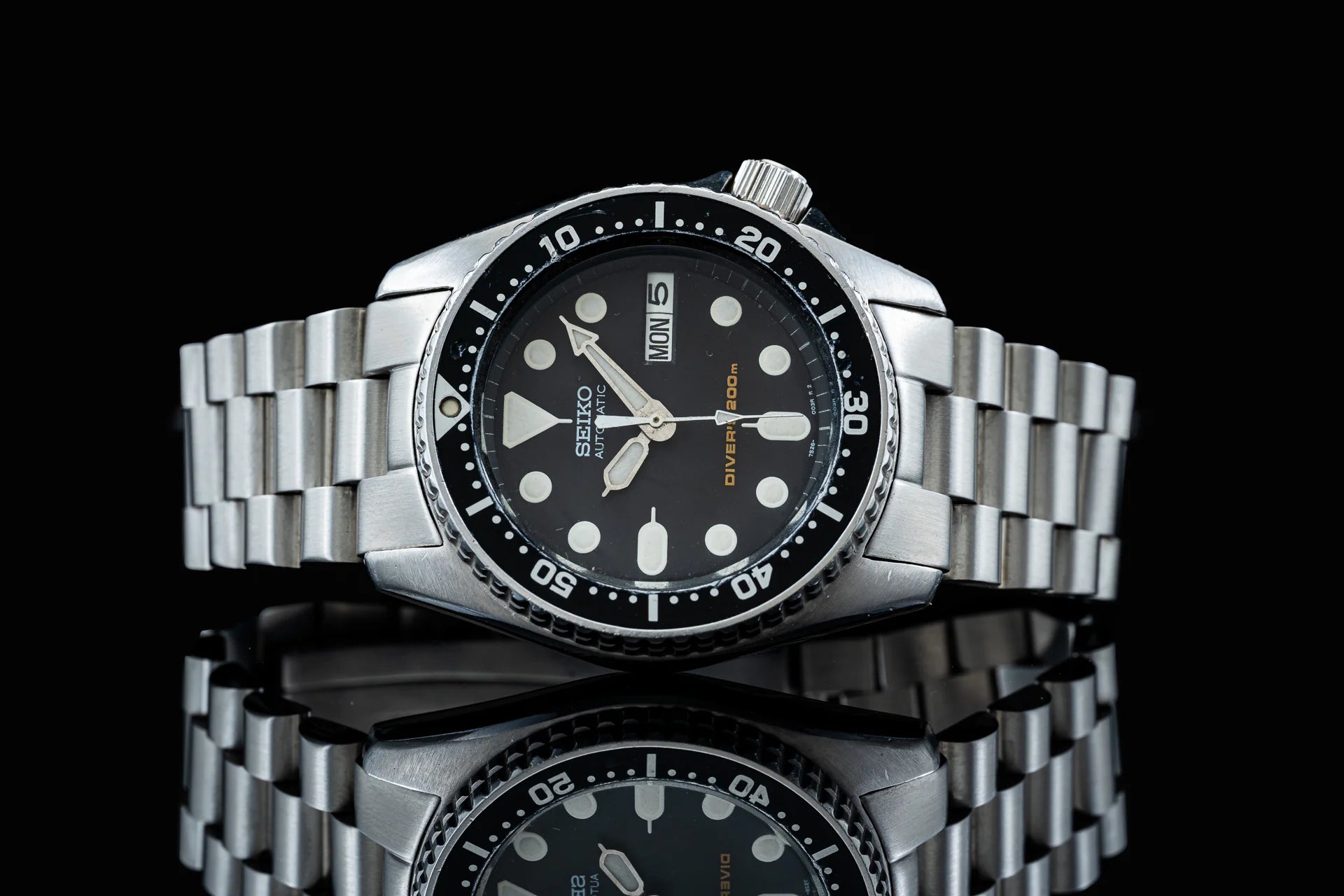 Seiko SKX013 automatic diver watch with stainless steel bracelet, black dial, and day-date window on black background