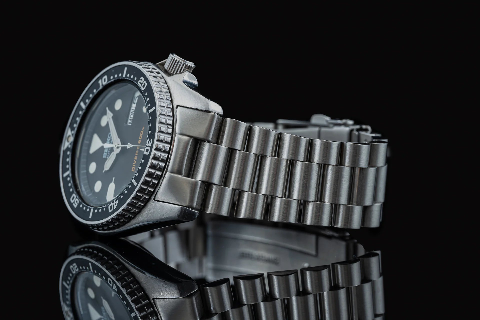 Seiko SKX013 dive watch with stainless steel bracelet and black dial on reflective surface