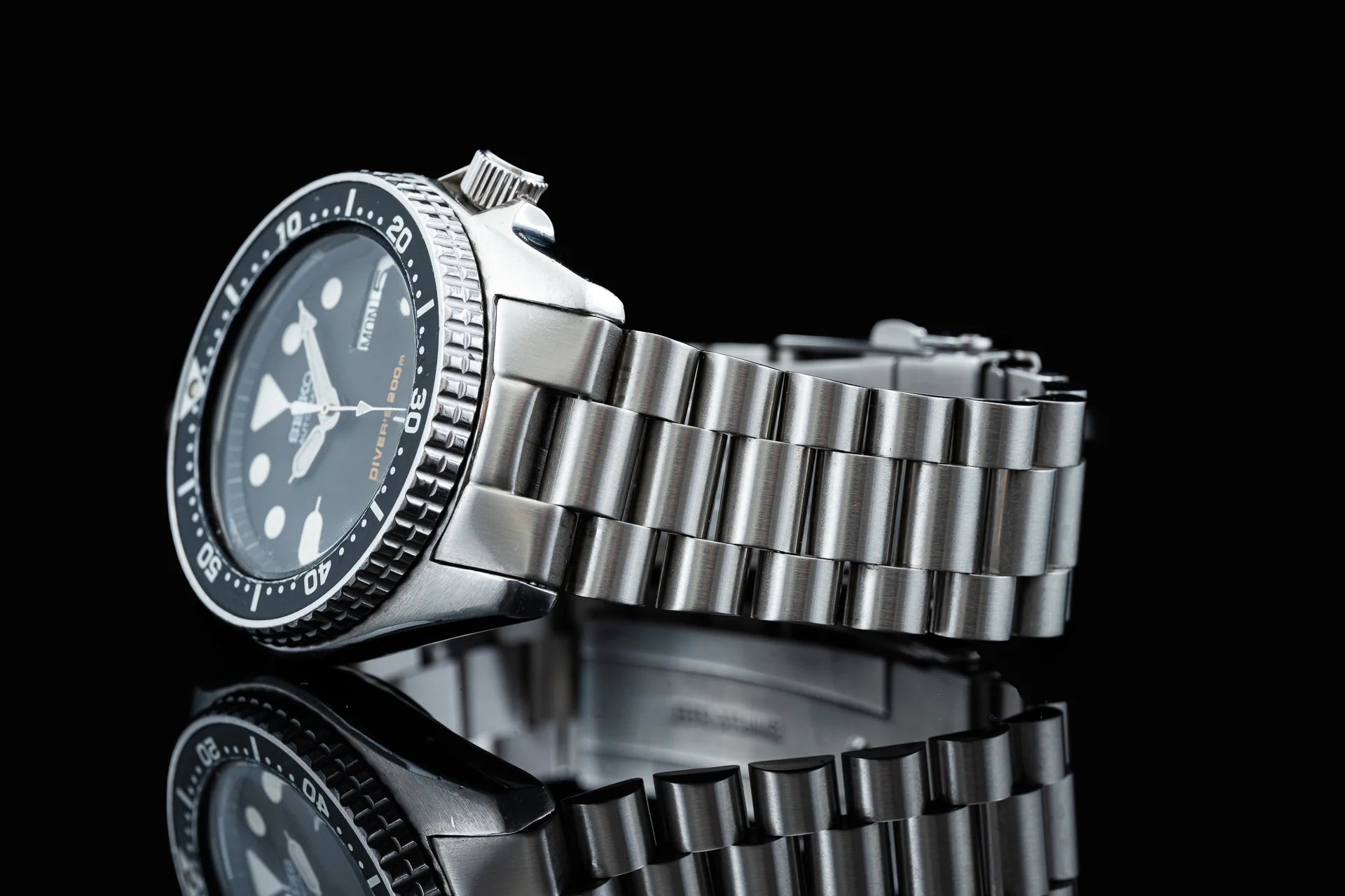 Seiko SKX013 stainless steel dive watch with black dial and three-link bracelet on black background