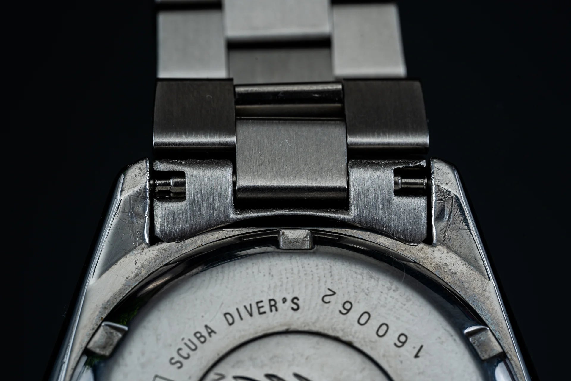 Seiko SKX013 dive watch with stainless steel bracelet and metal links, closeup of case back showing Scuba Diver engraving on black background