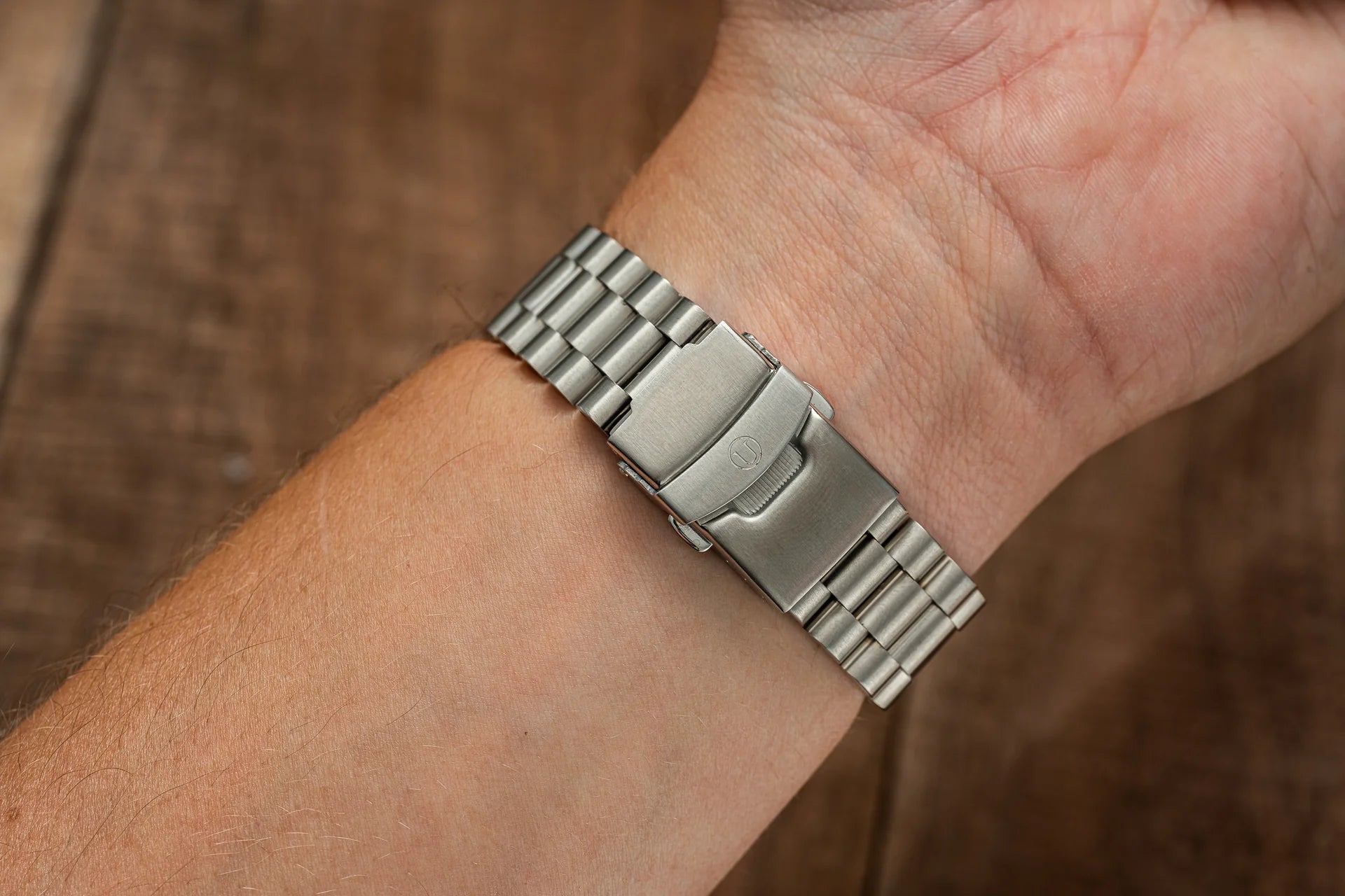 Stainless steel watch bracelet with solid link design and fold-over clasp worn on wrist