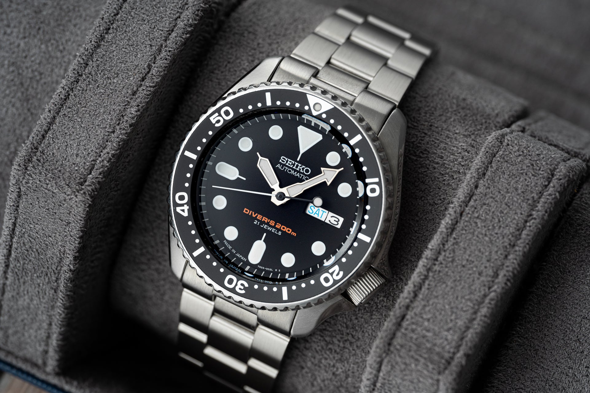 Seiko SKX007 automatic dive watch with stainless steel bracelet, black dial, and 200m water resistance on gray fabric background