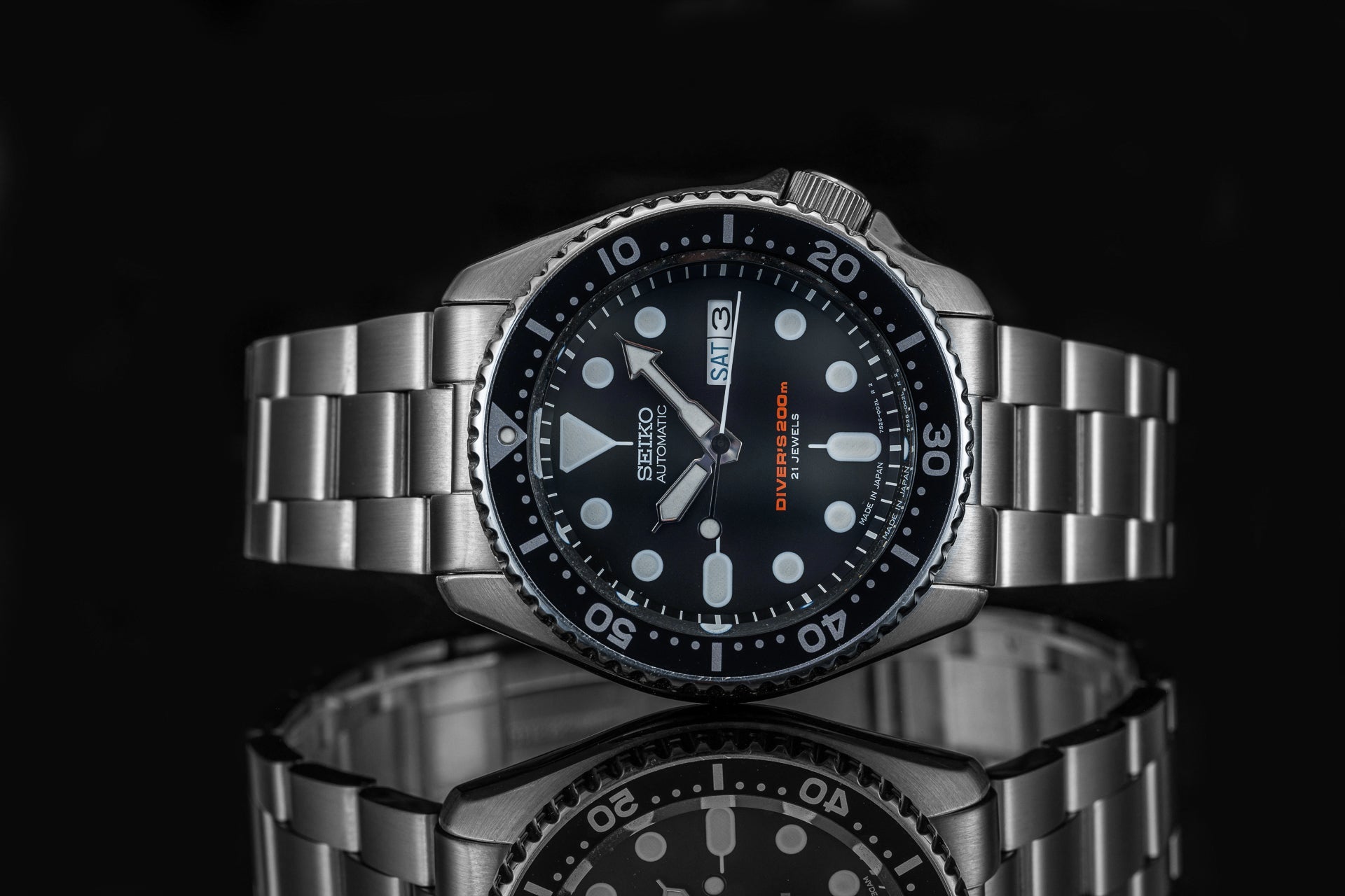Seiko SKX007 automatic dive watch with black dial, stainless steel bracelet and rotating bezel on reflective surface