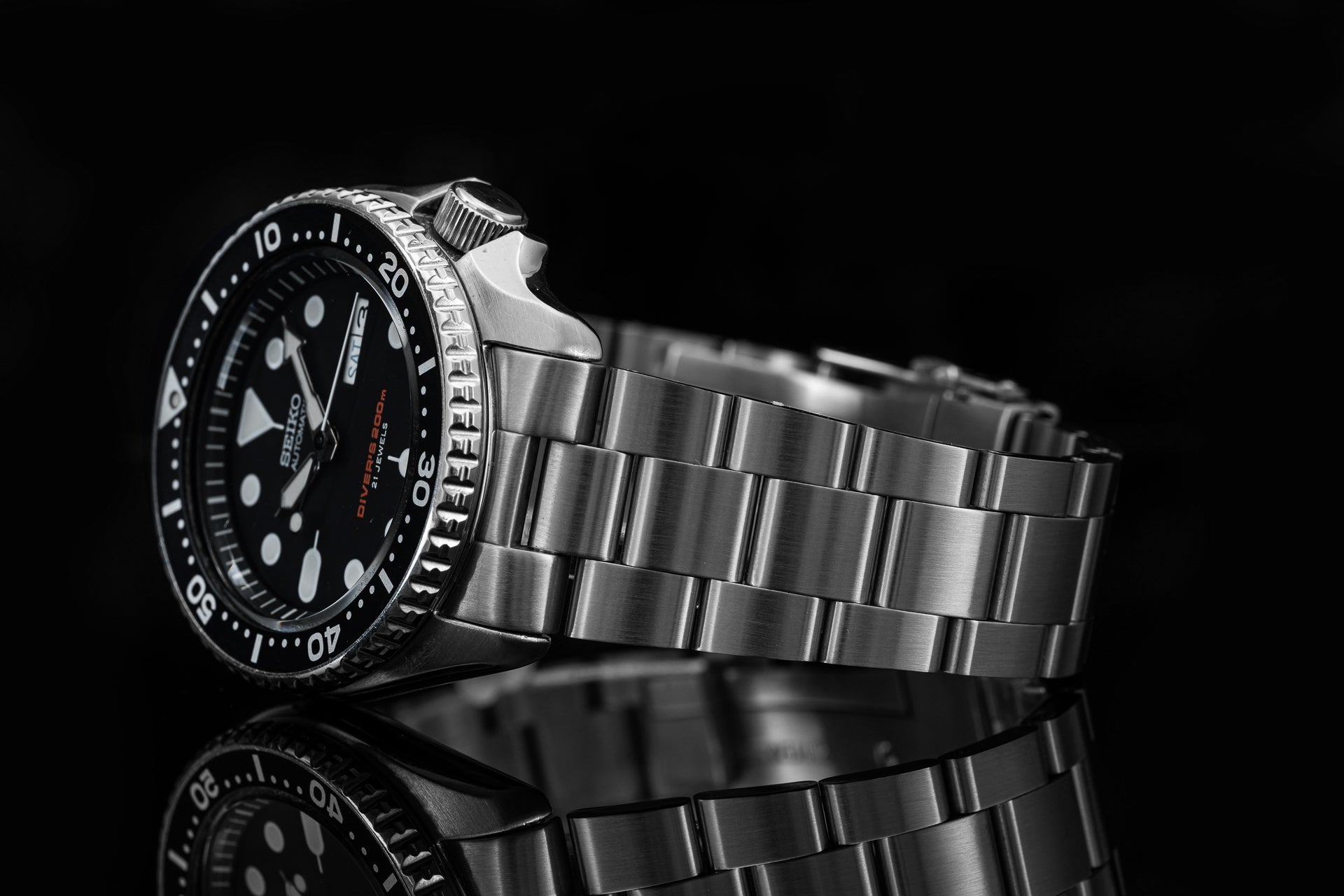 Seiko SKX007 dive watch with black dial, rotating bezel, and stainless steel bracelet on reflective surface