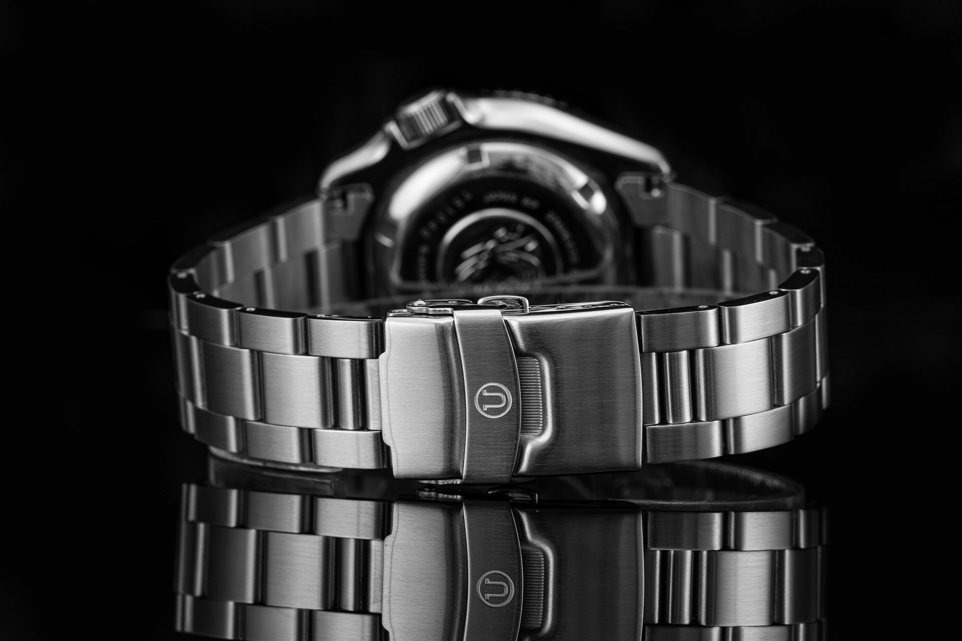 Stainless steel dive watch with metal bracelet and fold-over clasp, displayed front view on black background with reflection