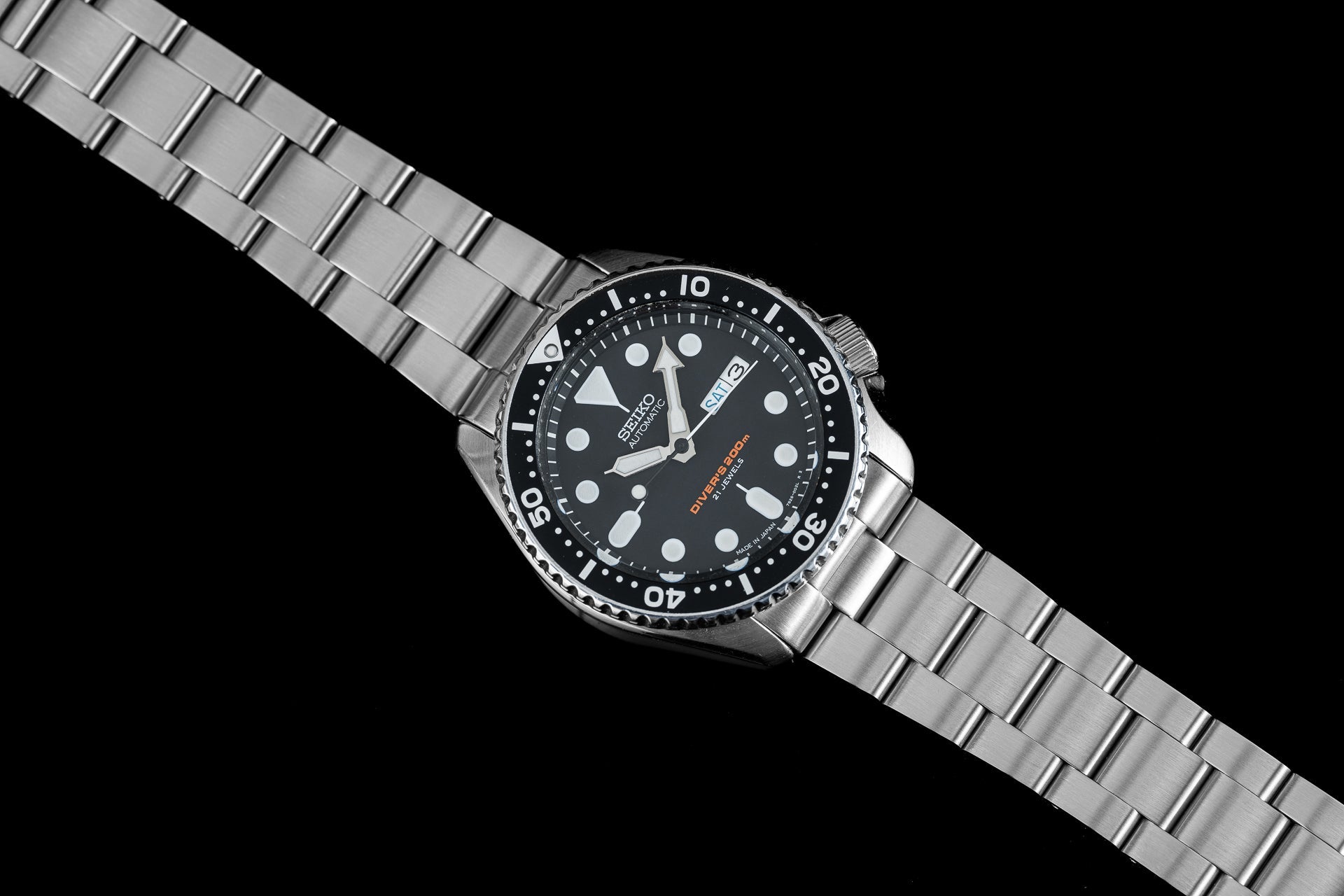 Seiko SKX007 dive watch with black dial, white hour markers, stainless steel bracelet and rotating bezel on black background