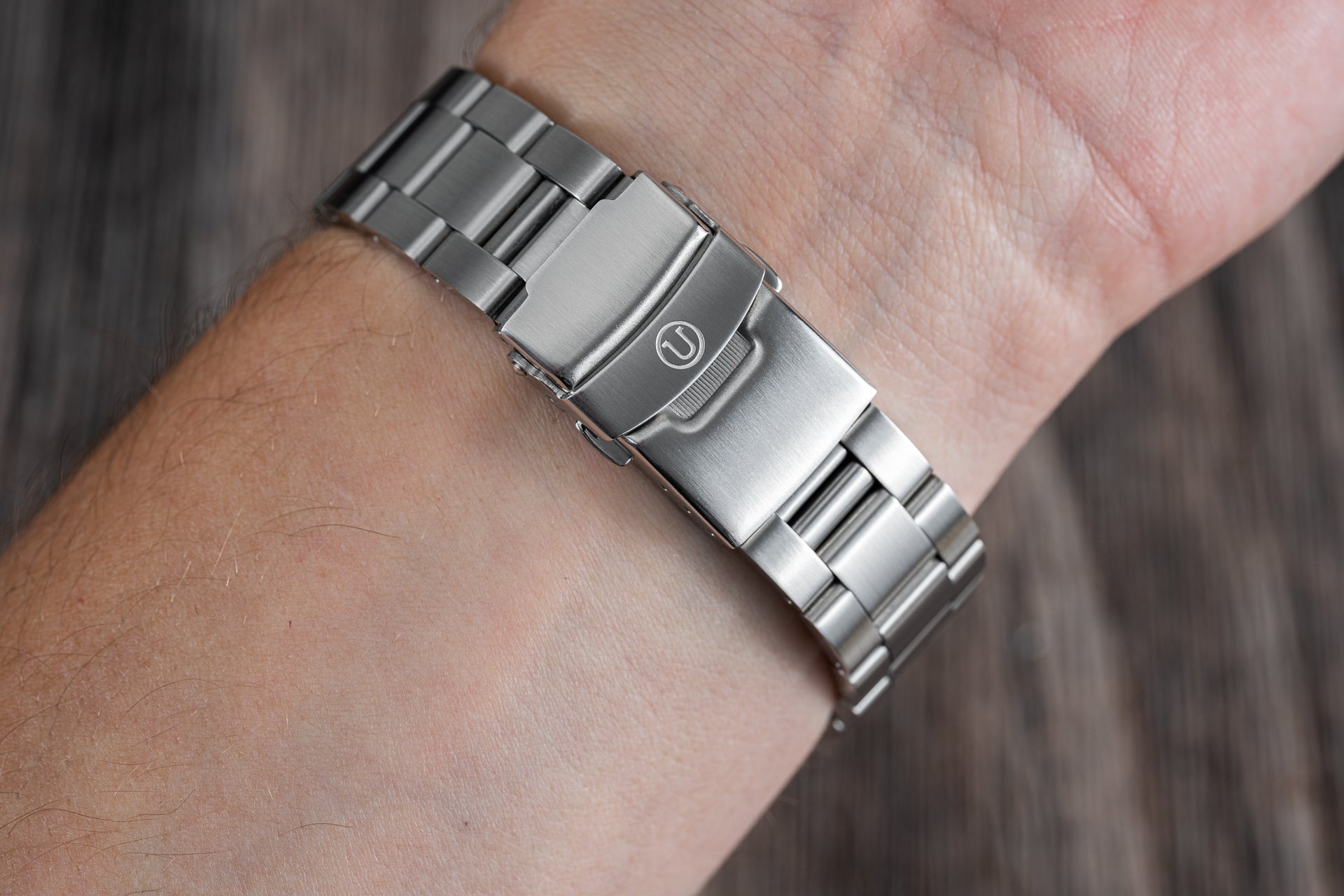 Stainless steel dive watch bracelet with solid link construction and secure clasp closure worn on wrist