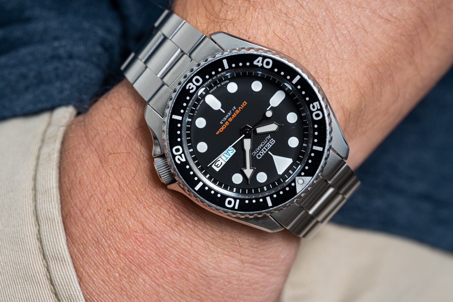 Stainless steel dive watch with black dial, white dot markers, and rotating bezel on man's wrist wearing blue shirt