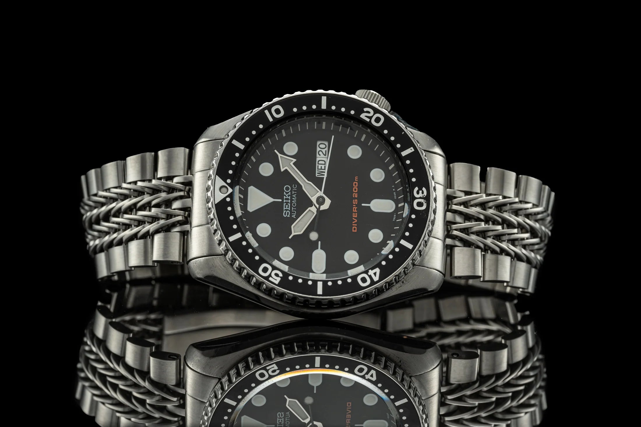 Seiko SKX007 automatic dive watch with black dial, stainless steel case, and twisted metal bracelet on black background