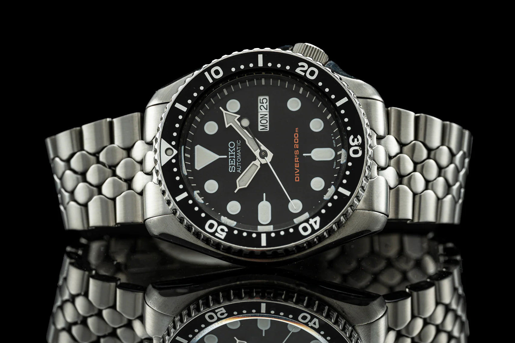 Seiko SKX007 diver watch with stainless steel bracelet, black dial, and rotating bezel on reflective surface