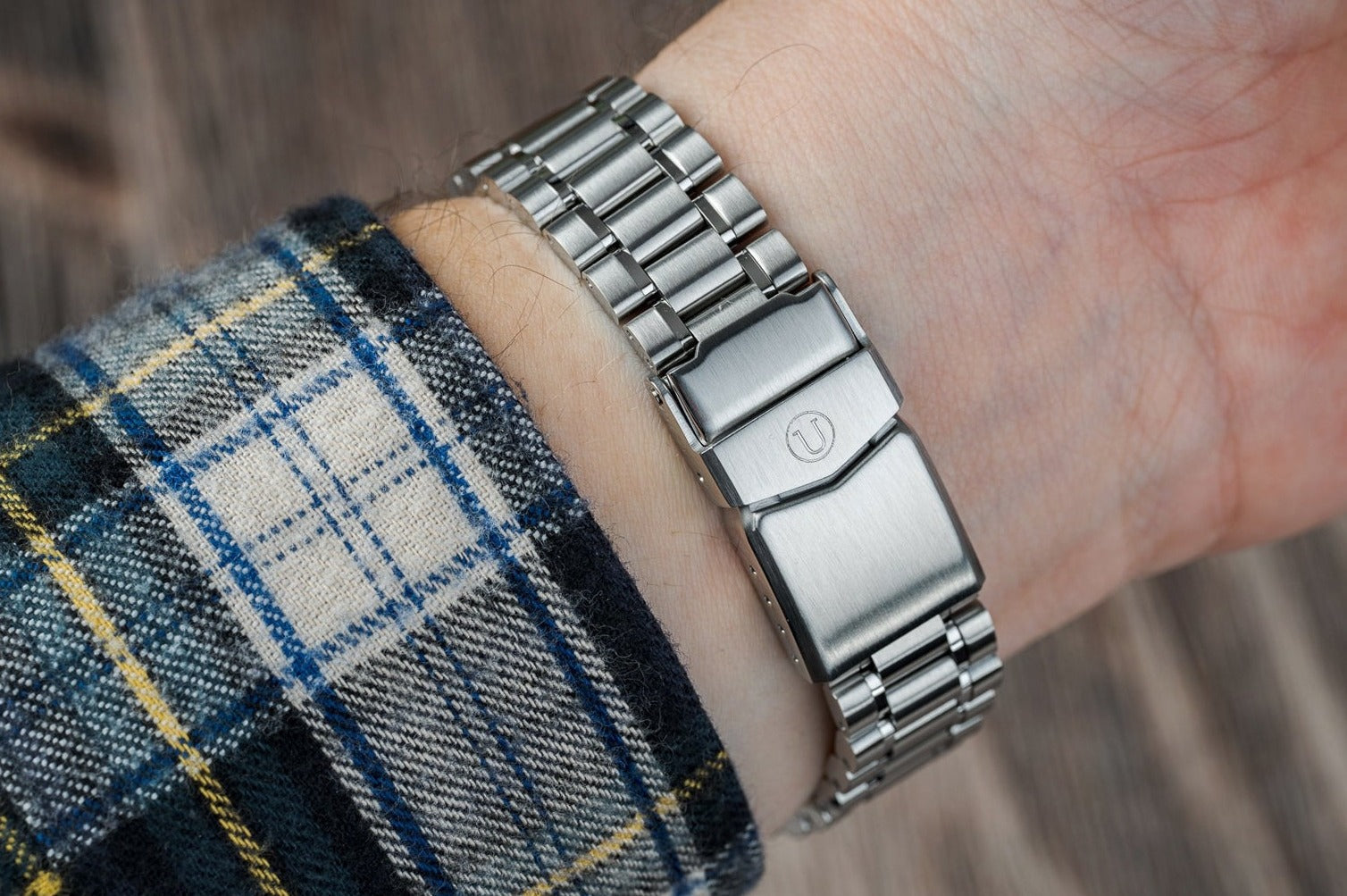 Stainless steel link bracelet with polished and brushed finish, worn on wrist with tartan fabric sleeve visible