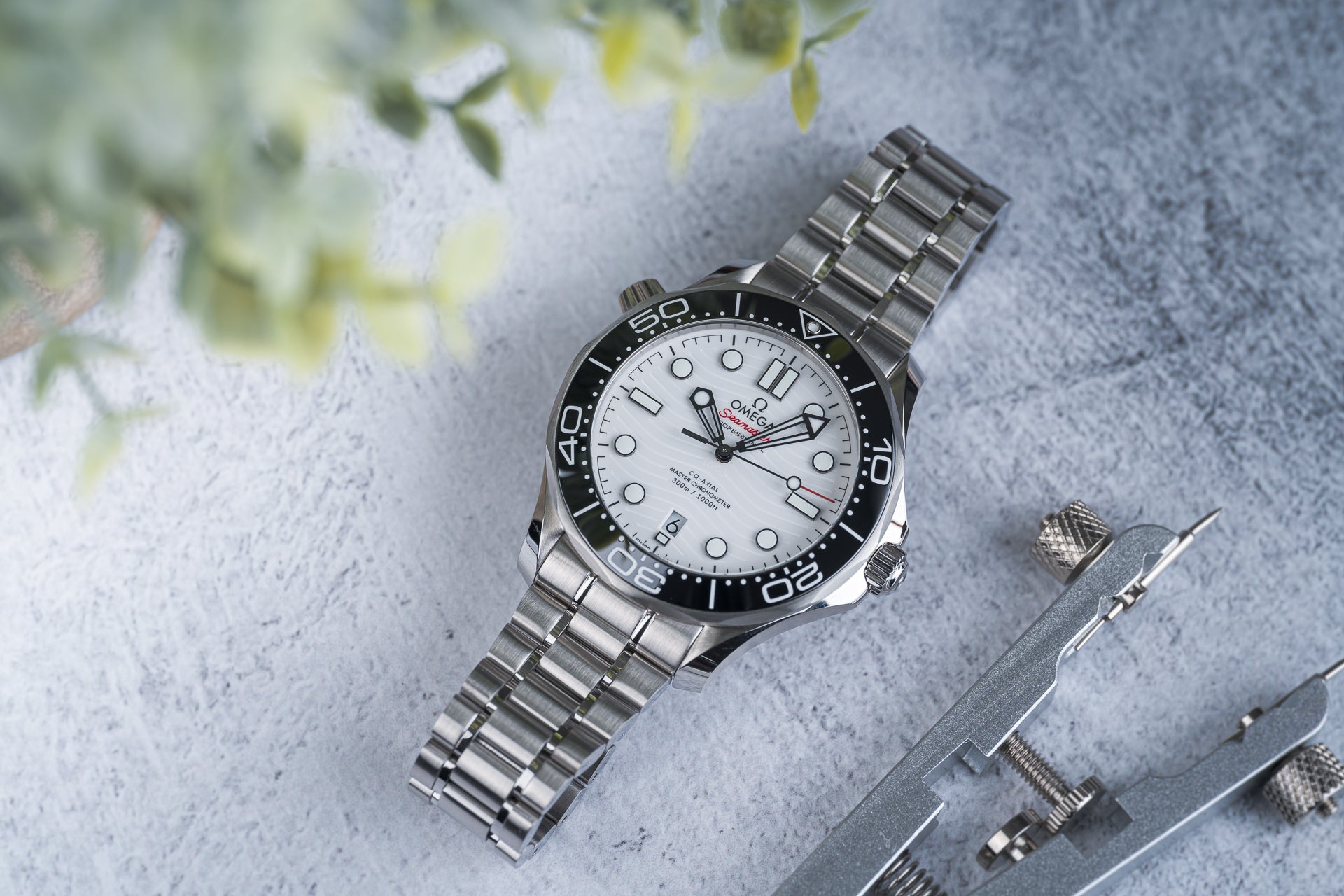 Omega Seamaster 300m stainless steel dive watch with white dial, black bezel, and metal bracelet on gray concrete background