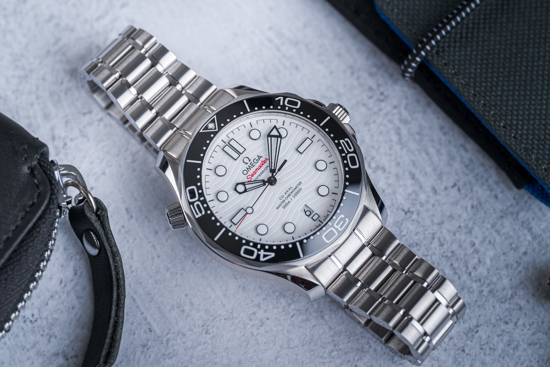 Omega Seamaster 300M stainless steel dive watch with white dial, black bezel, and matching metal bracelet on gray surface