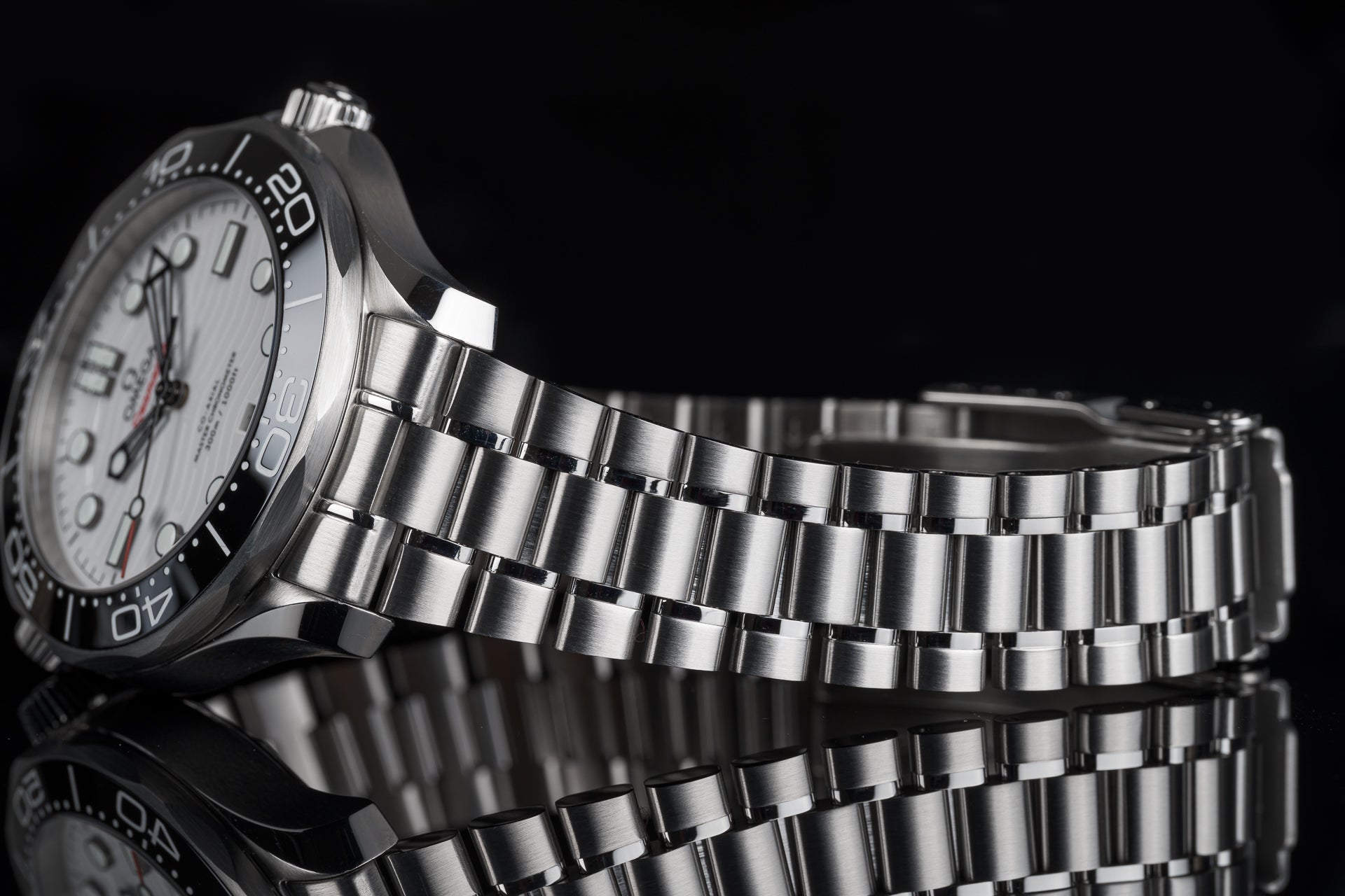 Stainless steel sports watch with white dial and metal bracelet on black background