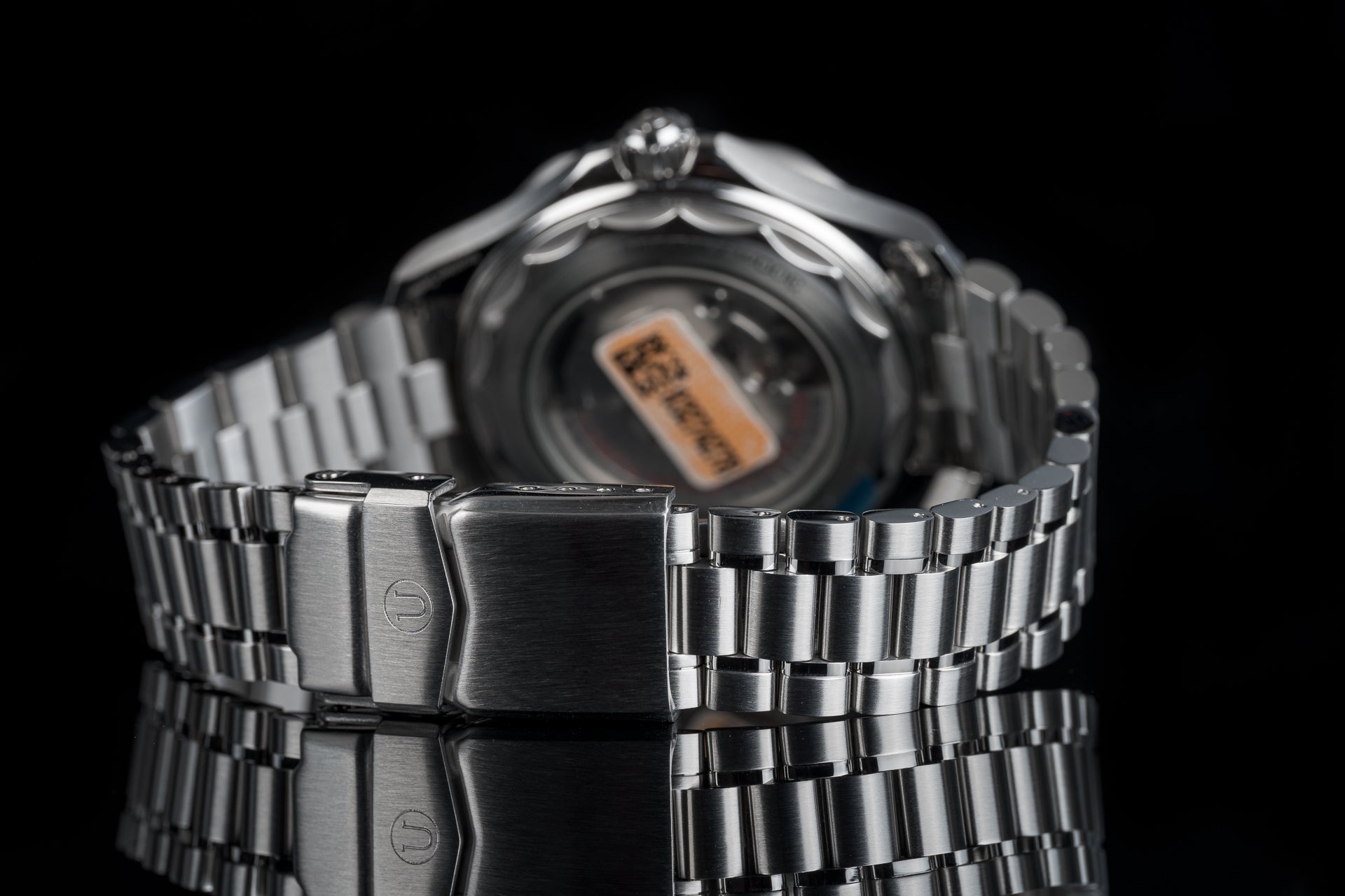 Stainless steel digital watch with metallic bracelet, orange LCD display, and fold-over clasp on black background