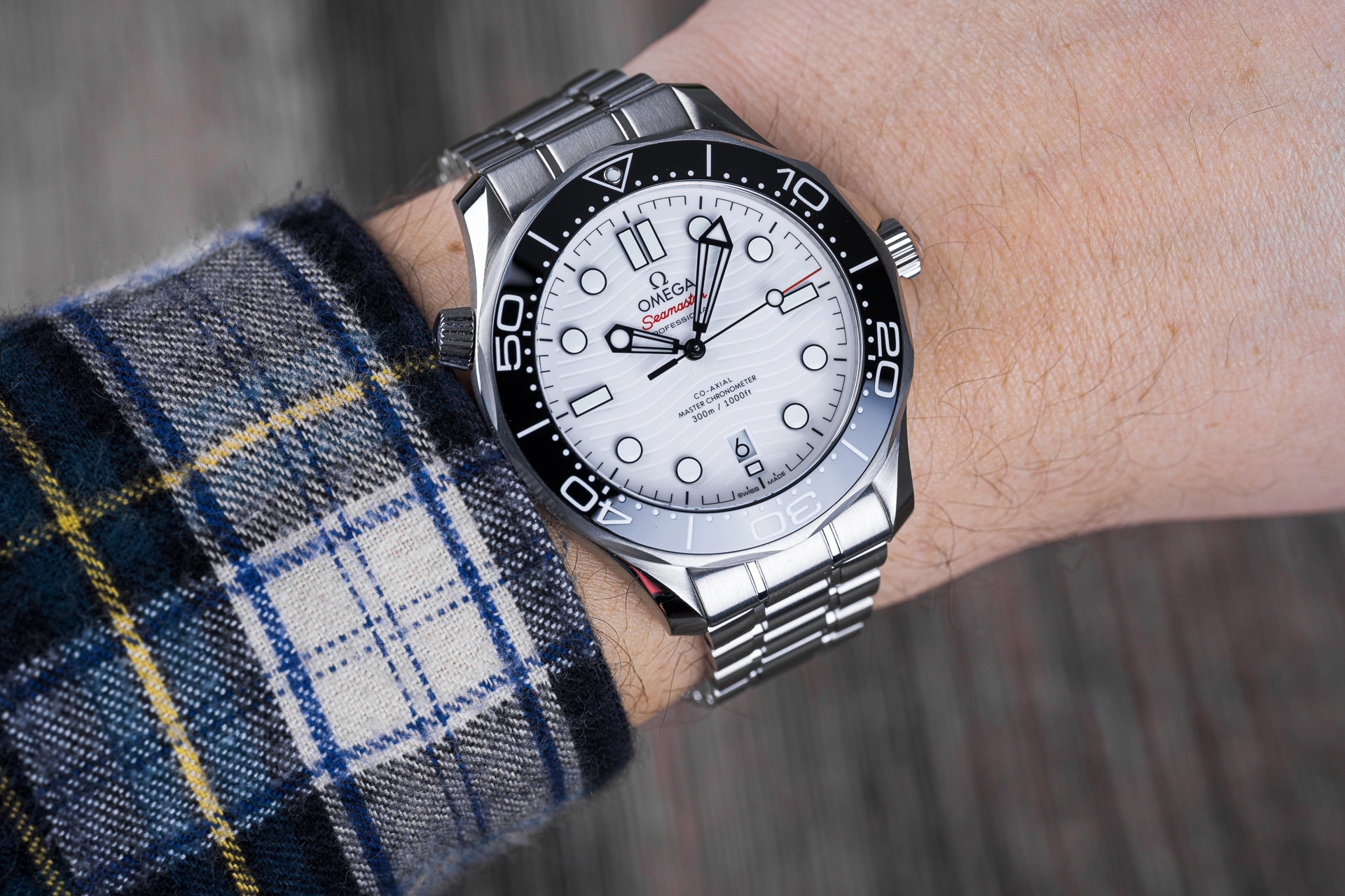 Omega Seamaster 300M dive watch with white dial, stainless steel bracelet and black bezel worn on wrist with plaid shirt sleeve