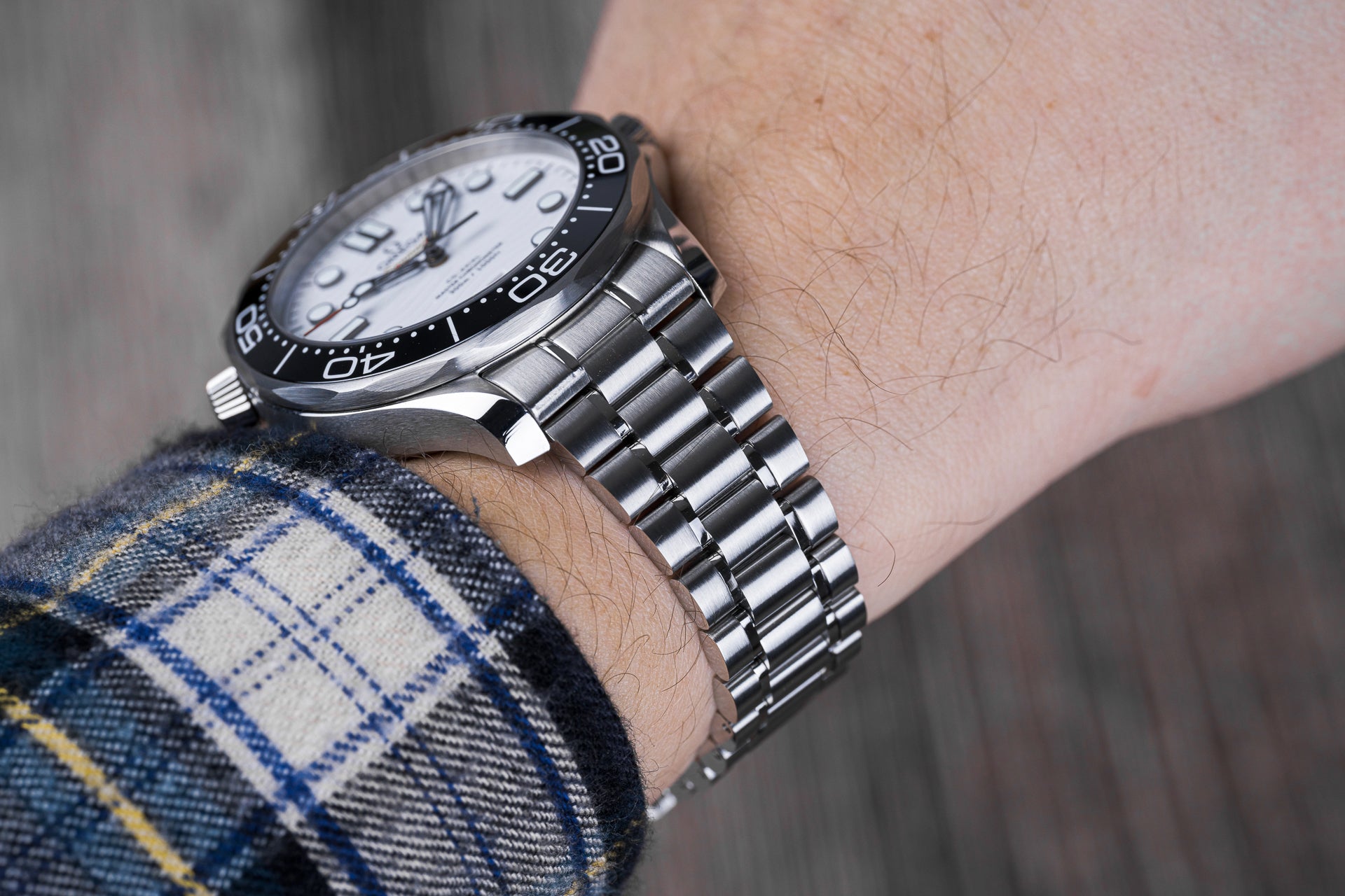 Stainless steel sports watch with white dial, black bezel, and metal bracelet worn on wrist with plaid shirt